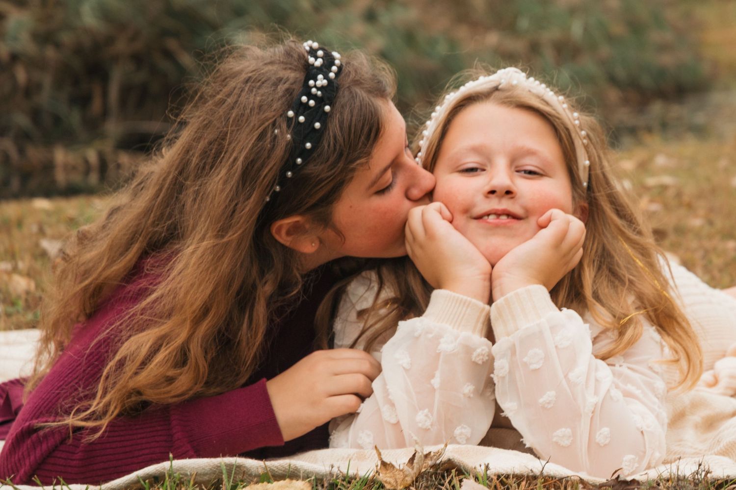 Two young sisters share a sweet moment as one kisses the other on the cheek outdoors.