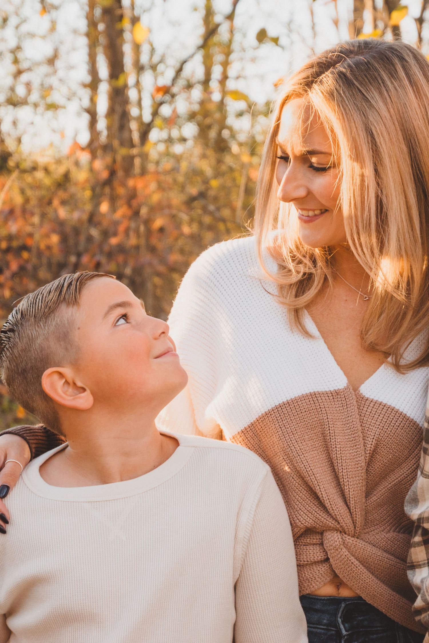 A young boy gazes up lovingly at his blonde mother during a golden autumn outdoor photo session.