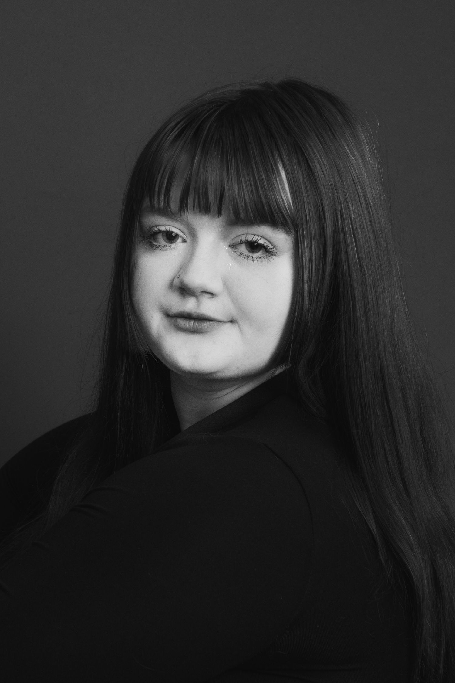 A black and white close-up portrait of a young woman with long straight bangs looking at the camera.