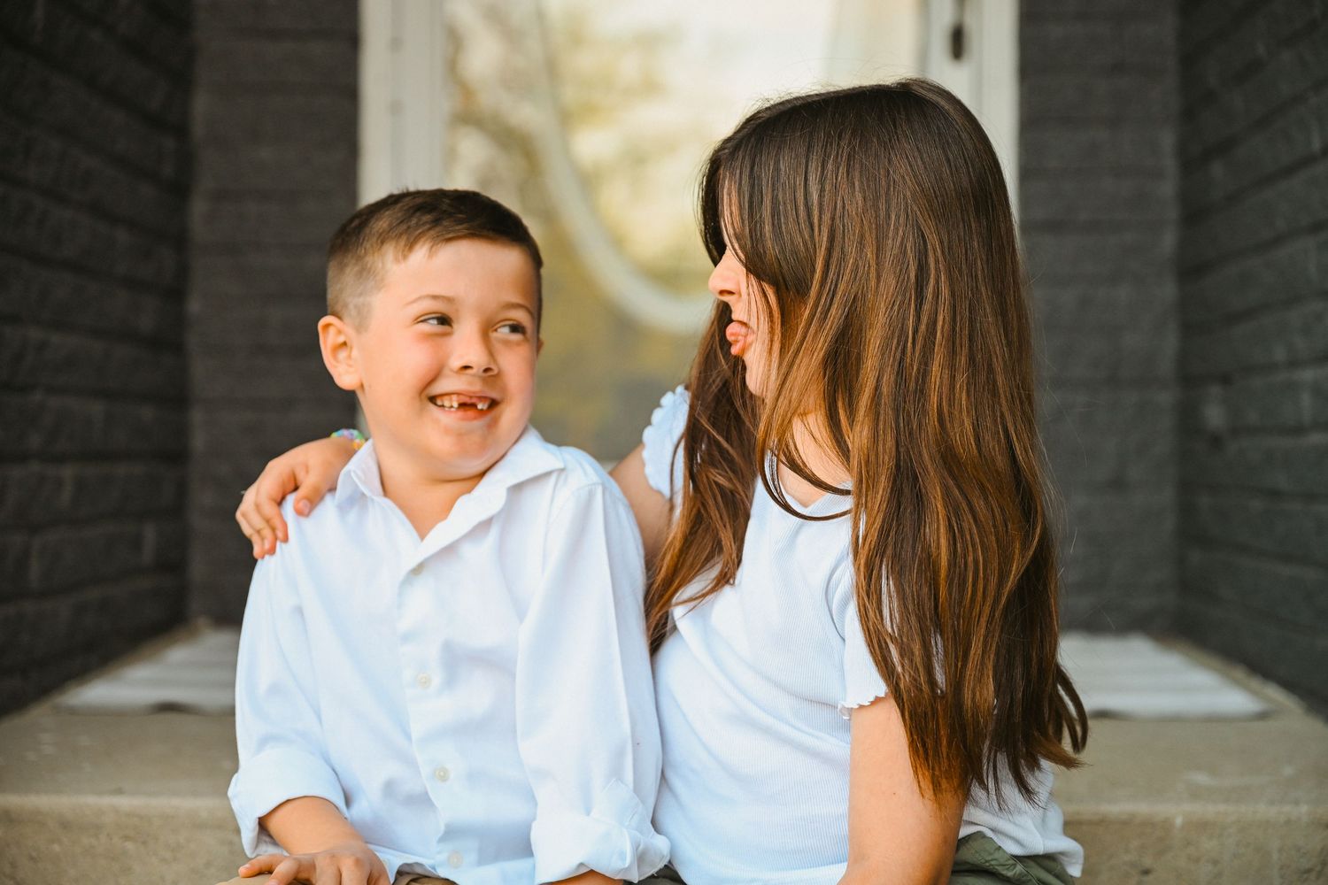 Young boy and girl in white shirts sitting on steps laughing and looking at each other.