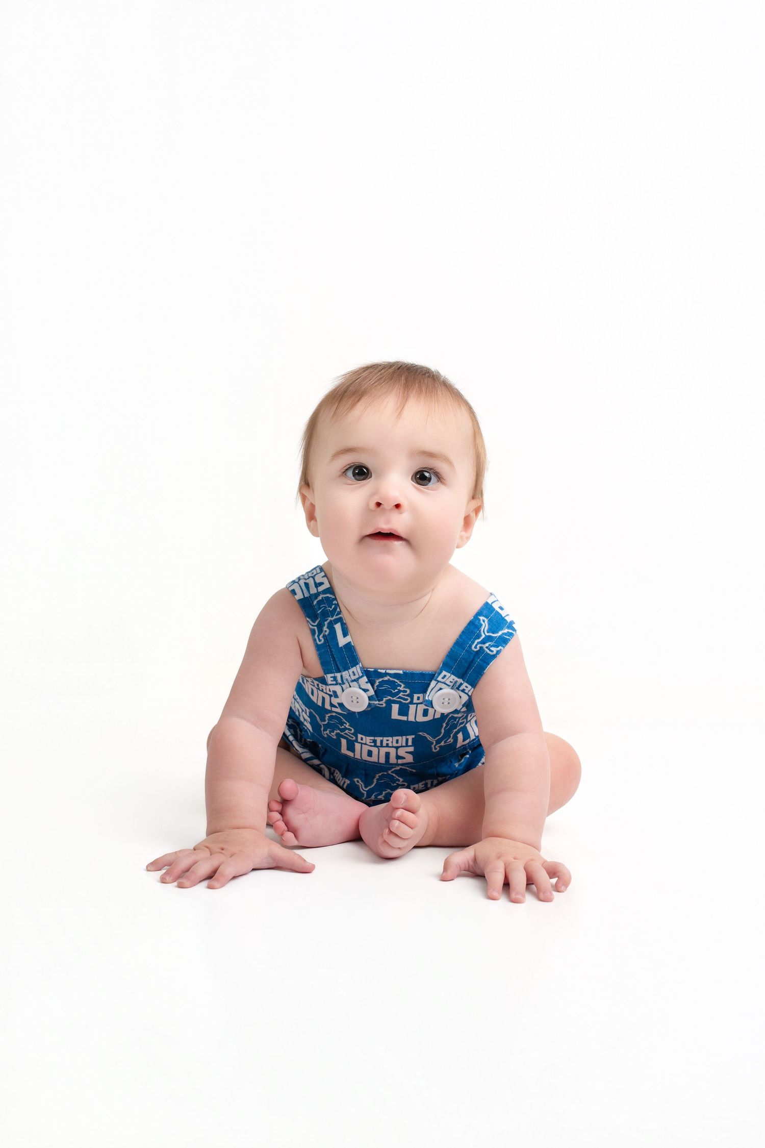 Baby sitting up wearing a Detroit Lions blue romper on a white background.