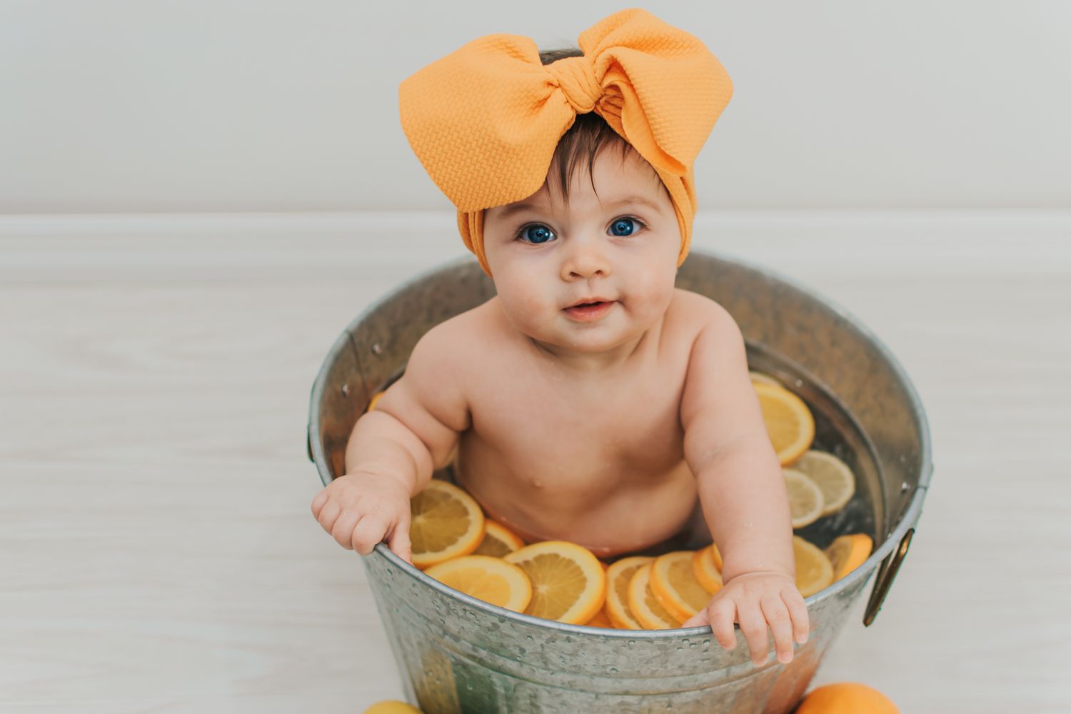 Six-month milestone studio session of a baby girl with a yellow bow, enjoying a fun fruit bath surrounded by fresh lemon slices