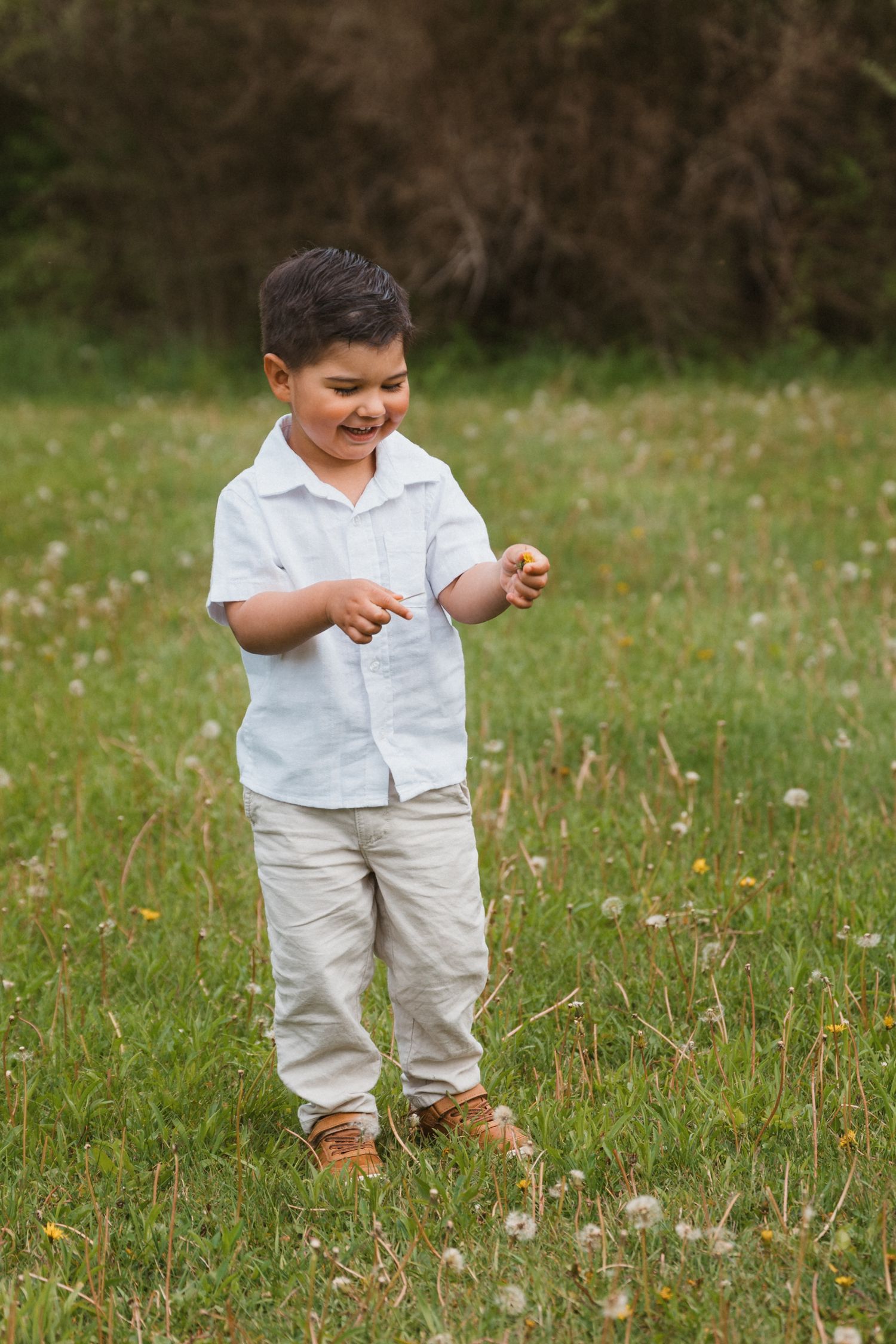 Happy young boy in white shirt smiling while playing in a green meadow outdoors.