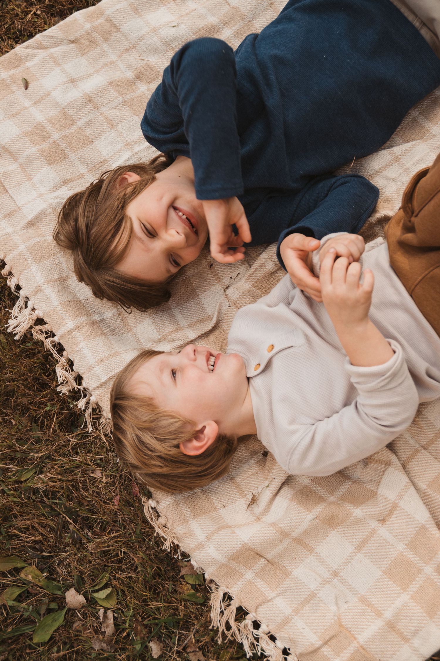 Two happy children laughing and playing together on a checkered blanket outside.