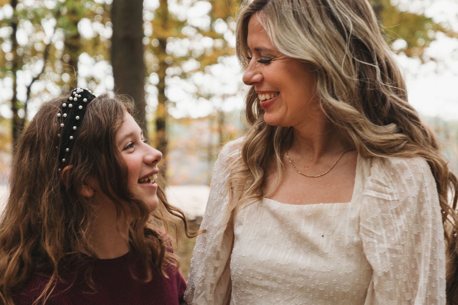 A brunette girl and her blonde mother share a joyful laughing moment together outdoors in autumn.