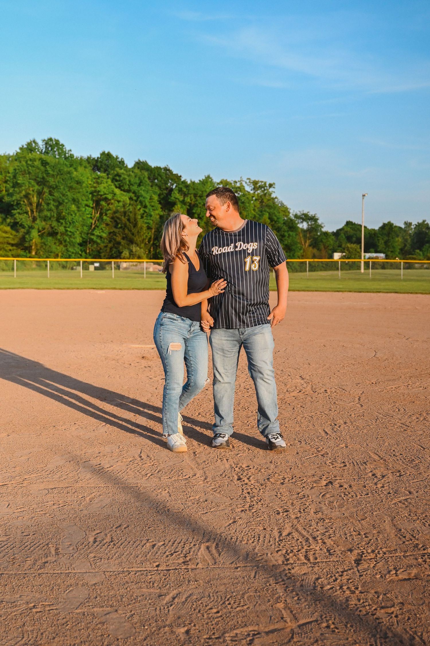 Couple sharing a romantic moment on a baseball diamond during golden hour sunset.