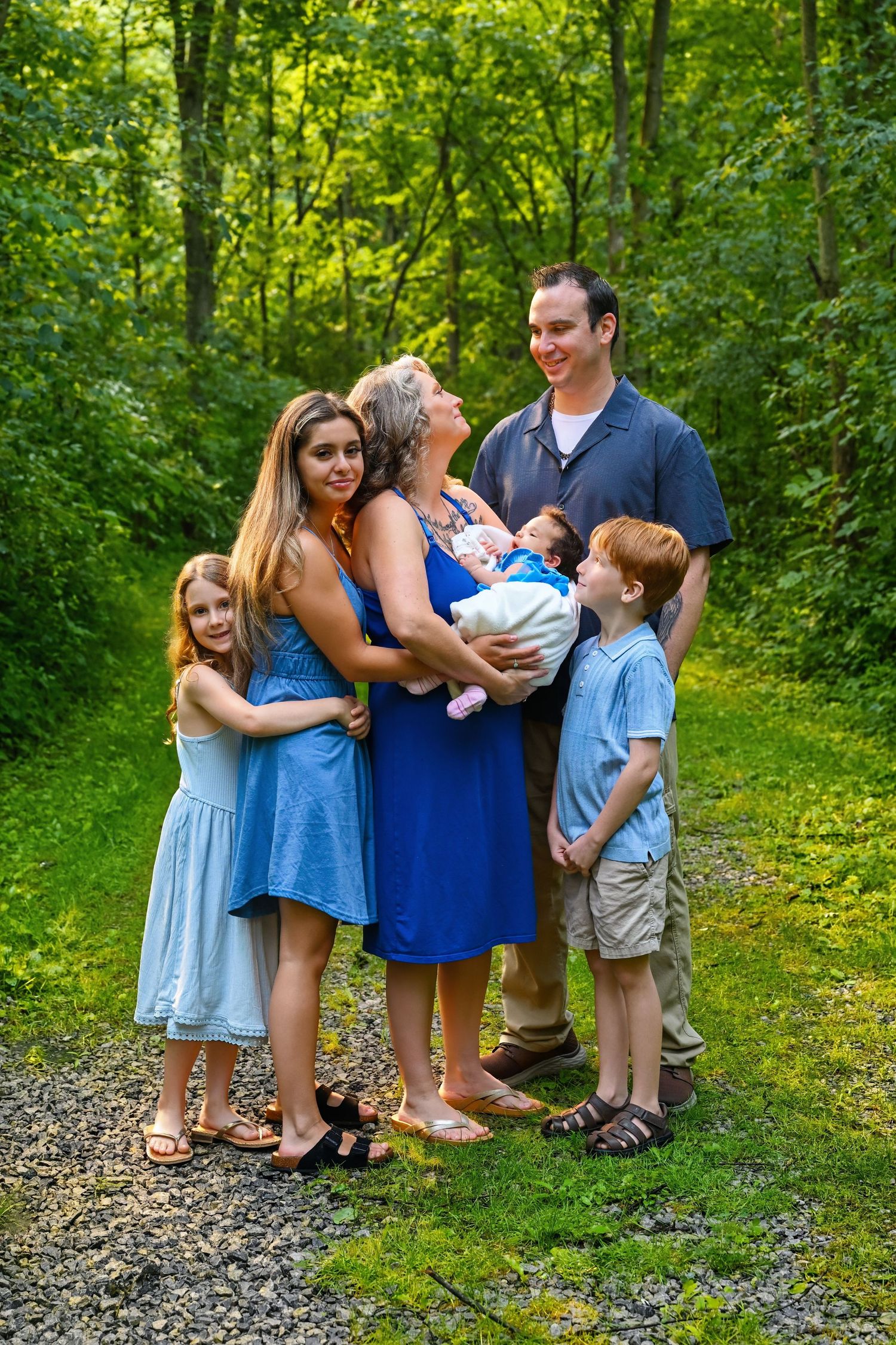 Family of six posing on a green forest path, mother holding newborn baby outdoors.