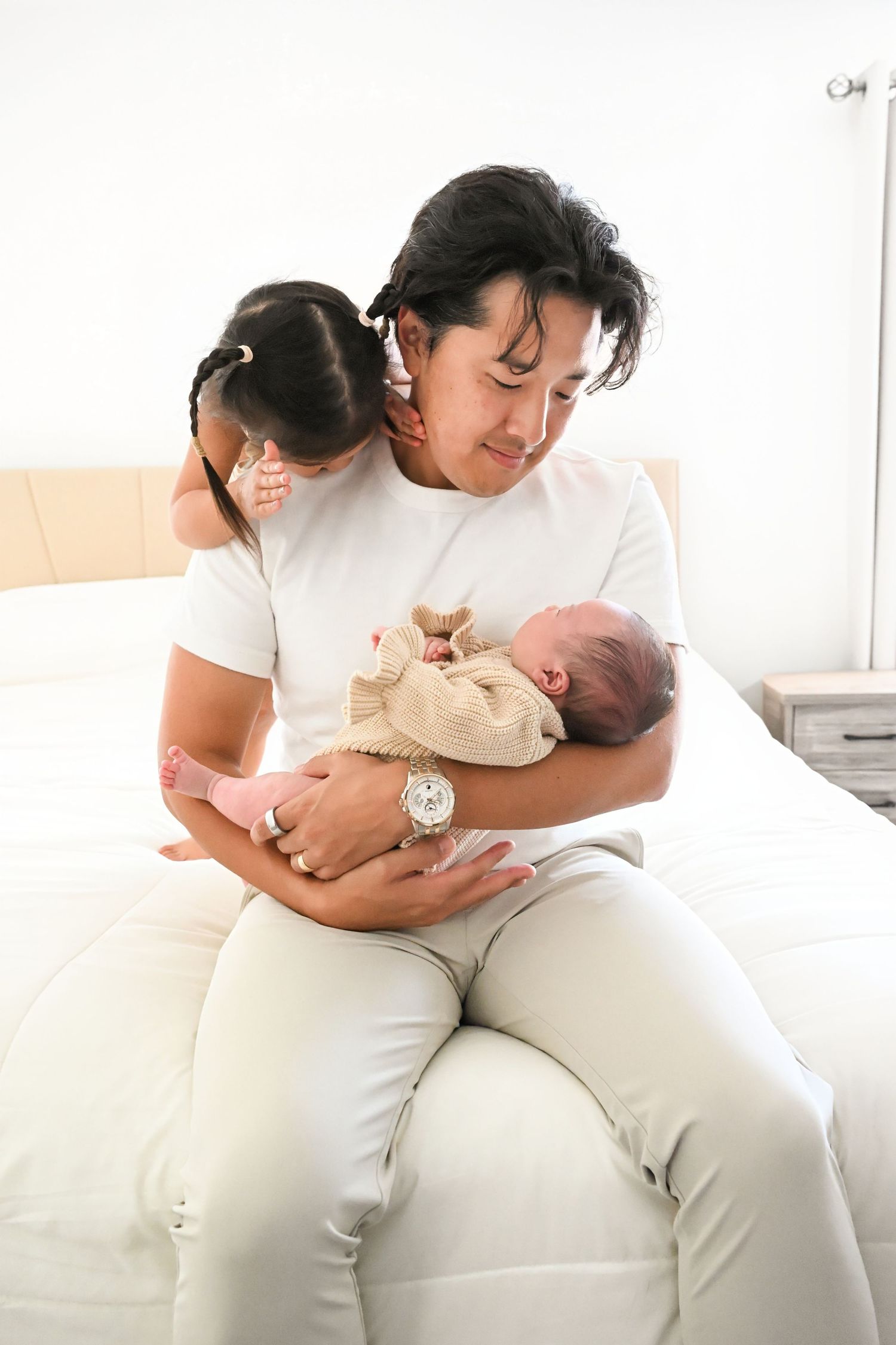 Toddler plays peek a boo over dad's shoulder with her new baby sister at their in home family session.