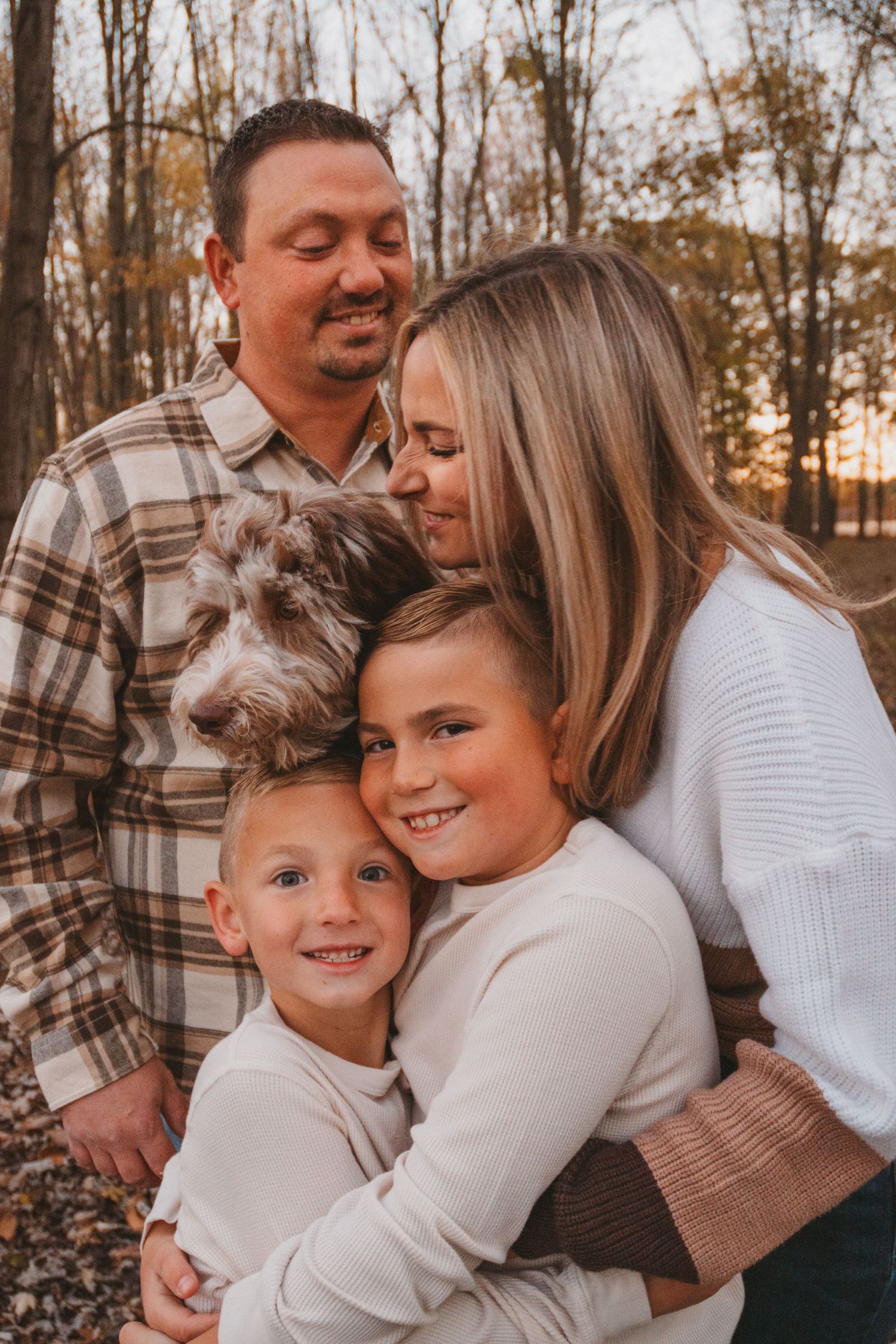 A smiling family of four with a small dog shares a warm embrace during an autumn outdoor photo session.