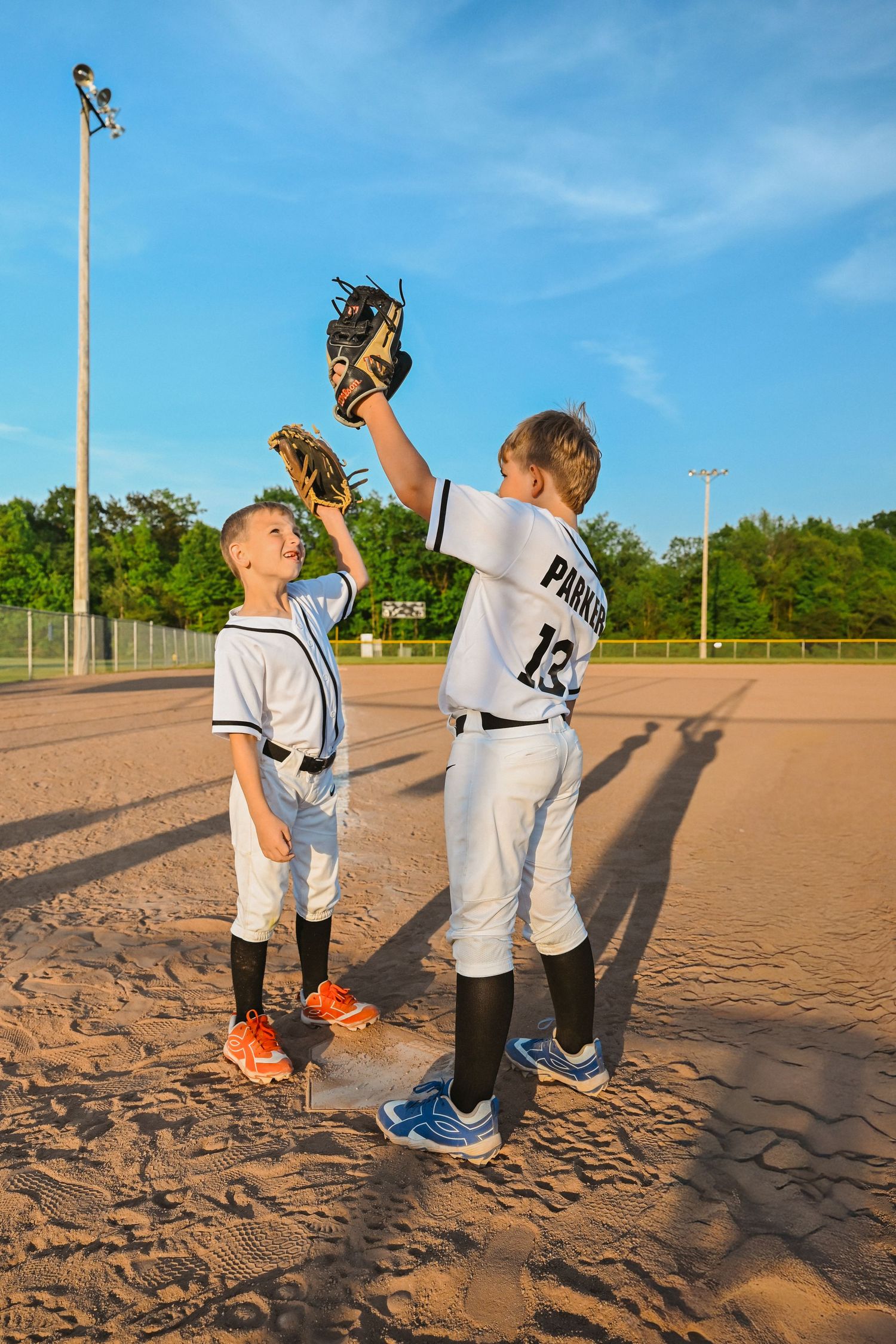 Two young baseball players on dirt field, one raising glove high in celebration.