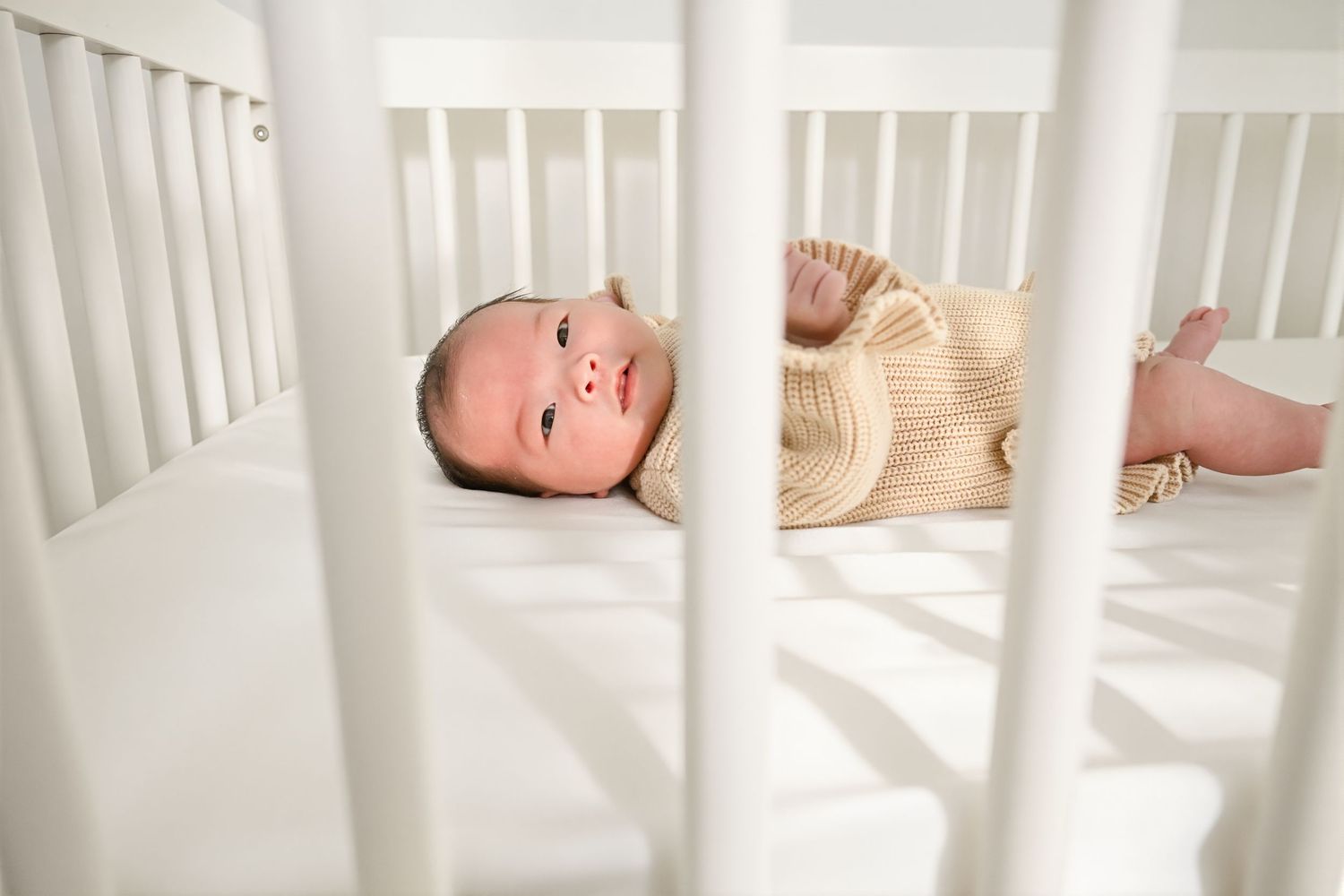 Newborn baby lays in her crib looking at the camera during her in home Newborn session in Macomb MI