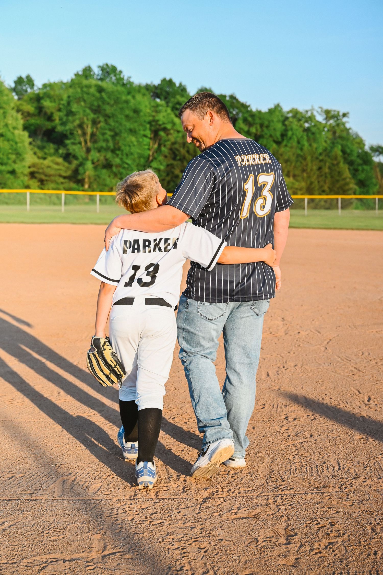 Father and son in matching number 13 Parker jerseys walking together on baseball field.
