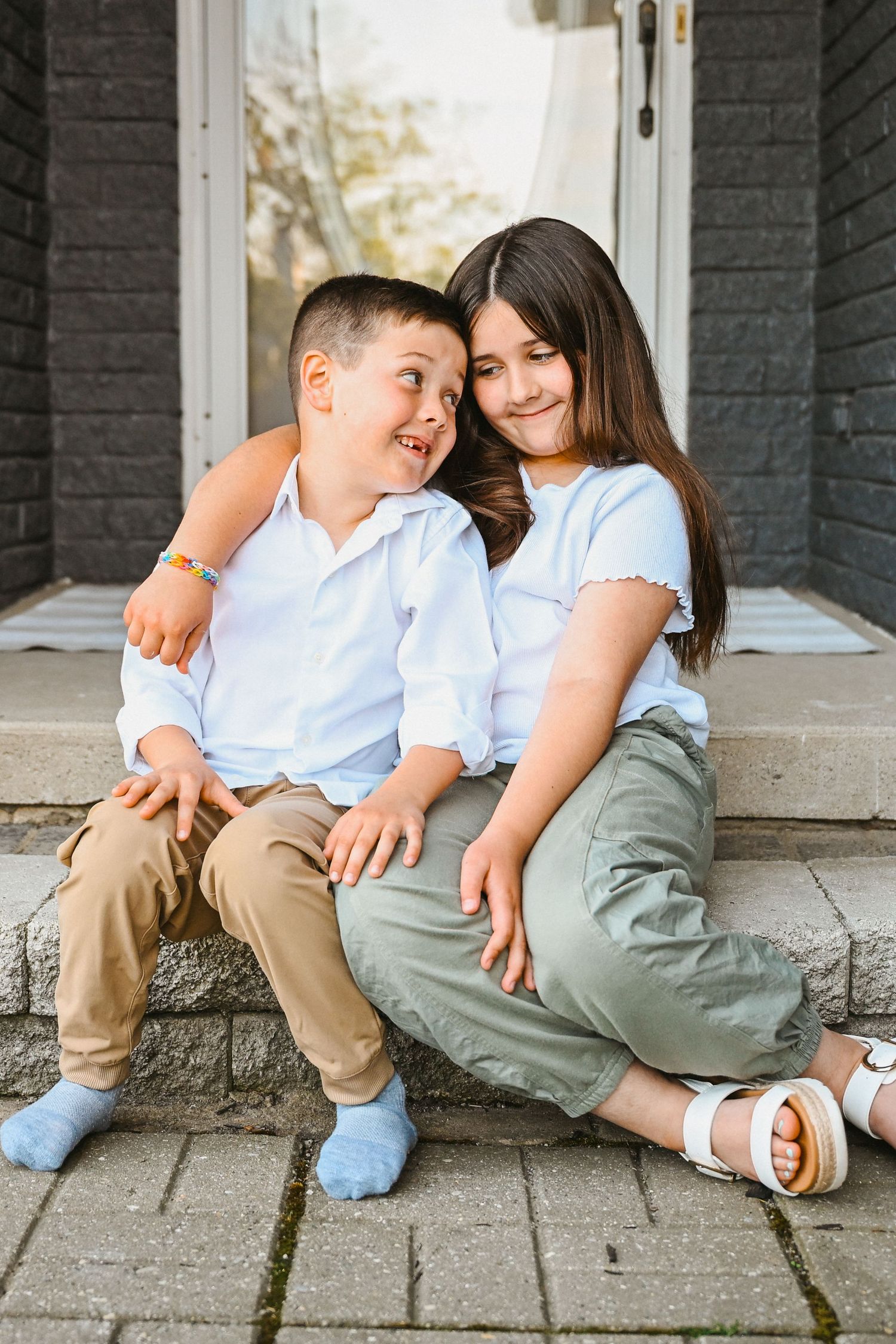 A boy and girl sitting on porch steps, laughing and hugging in casual outfits outdoors.
