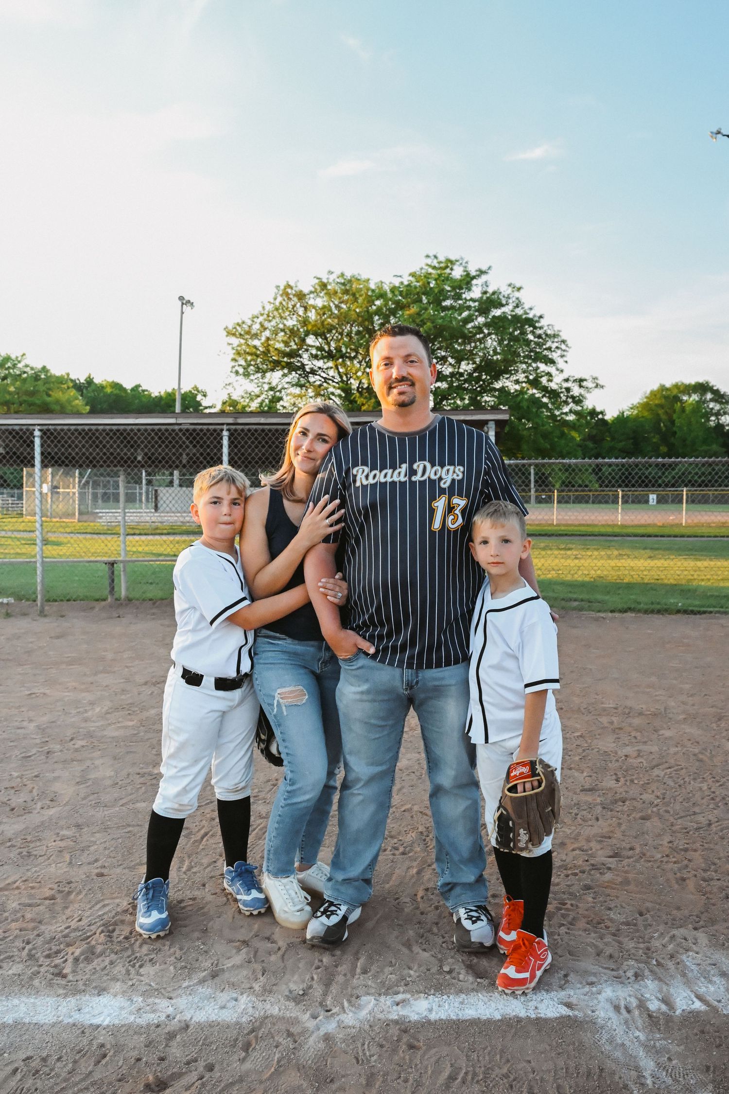 Family portrait on baseball field, father in Road Dogs jersey with two boys in uniforms.