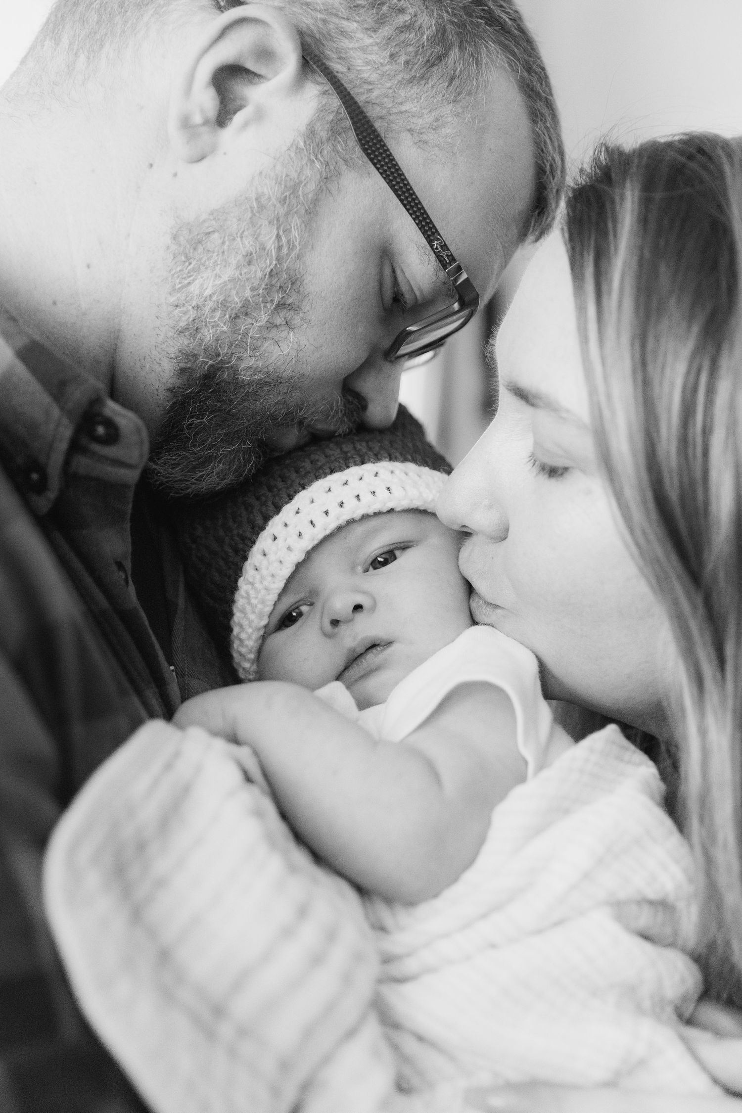Black and white series of intimate family moments showing parents sharing tender kisses with their sleeping newborn.