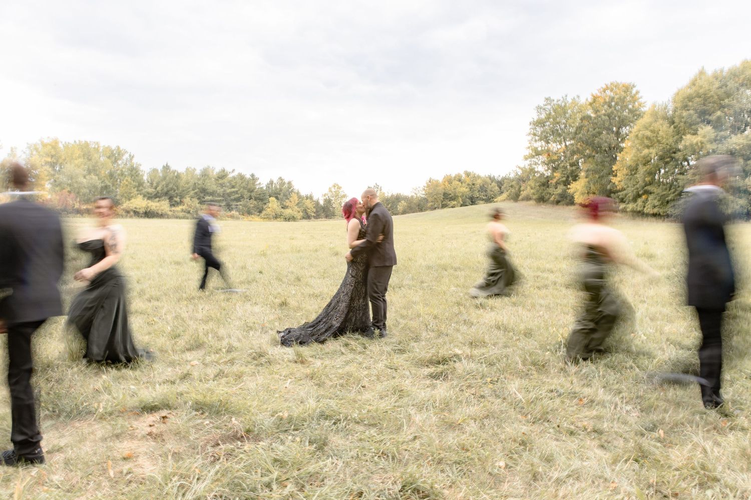 Motion blur captures people dancing in a grassy field with trees in the background.