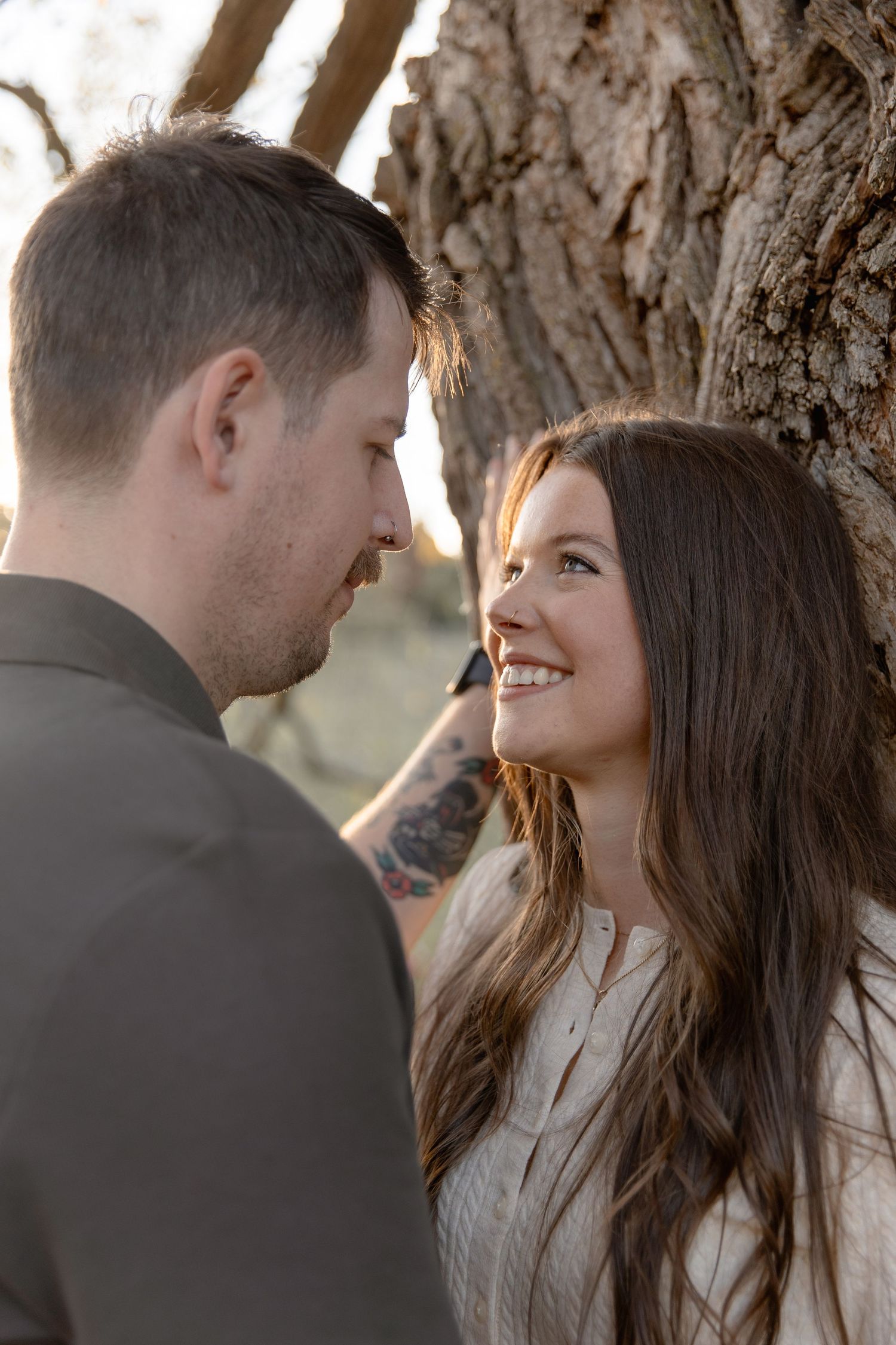 A couple shares tender moments near a large tree trunk during an outdoor photoshoot.