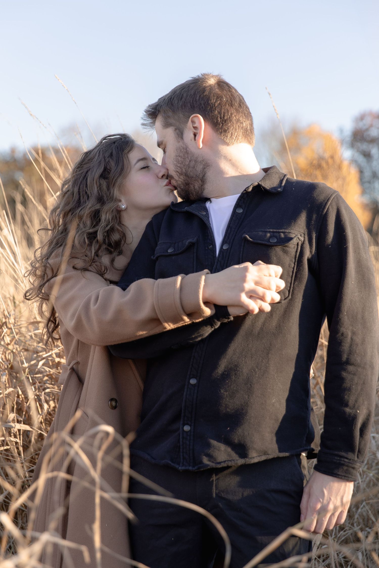 A romantic couple shares an intimate moment while embracing in a field of tall grass during golden hour.