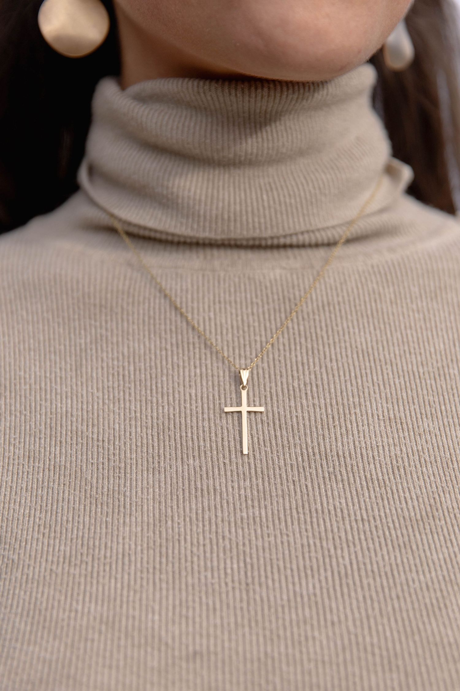 A series of close-up shots showing different delicate gold cross and religious pendant necklaces on a beige turtleneck.