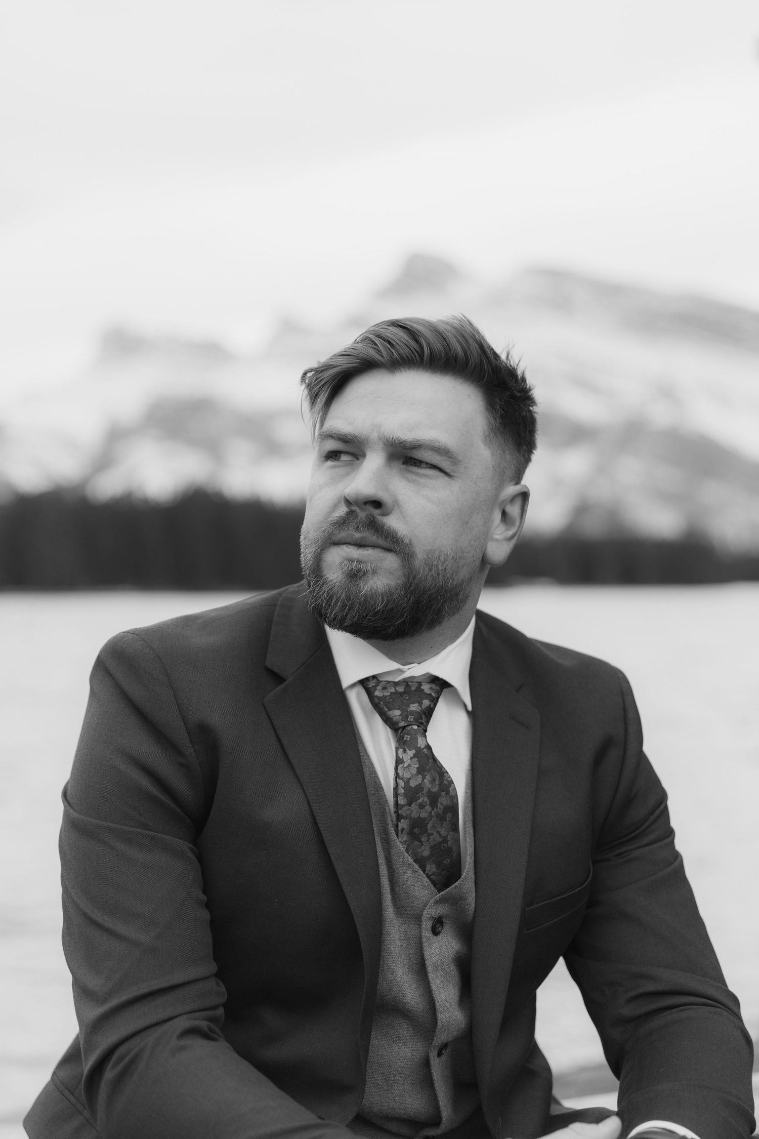 Black and white photo series of a bearded man in a suit and tie looking thoughtfully to the side against a scenic backdrop.