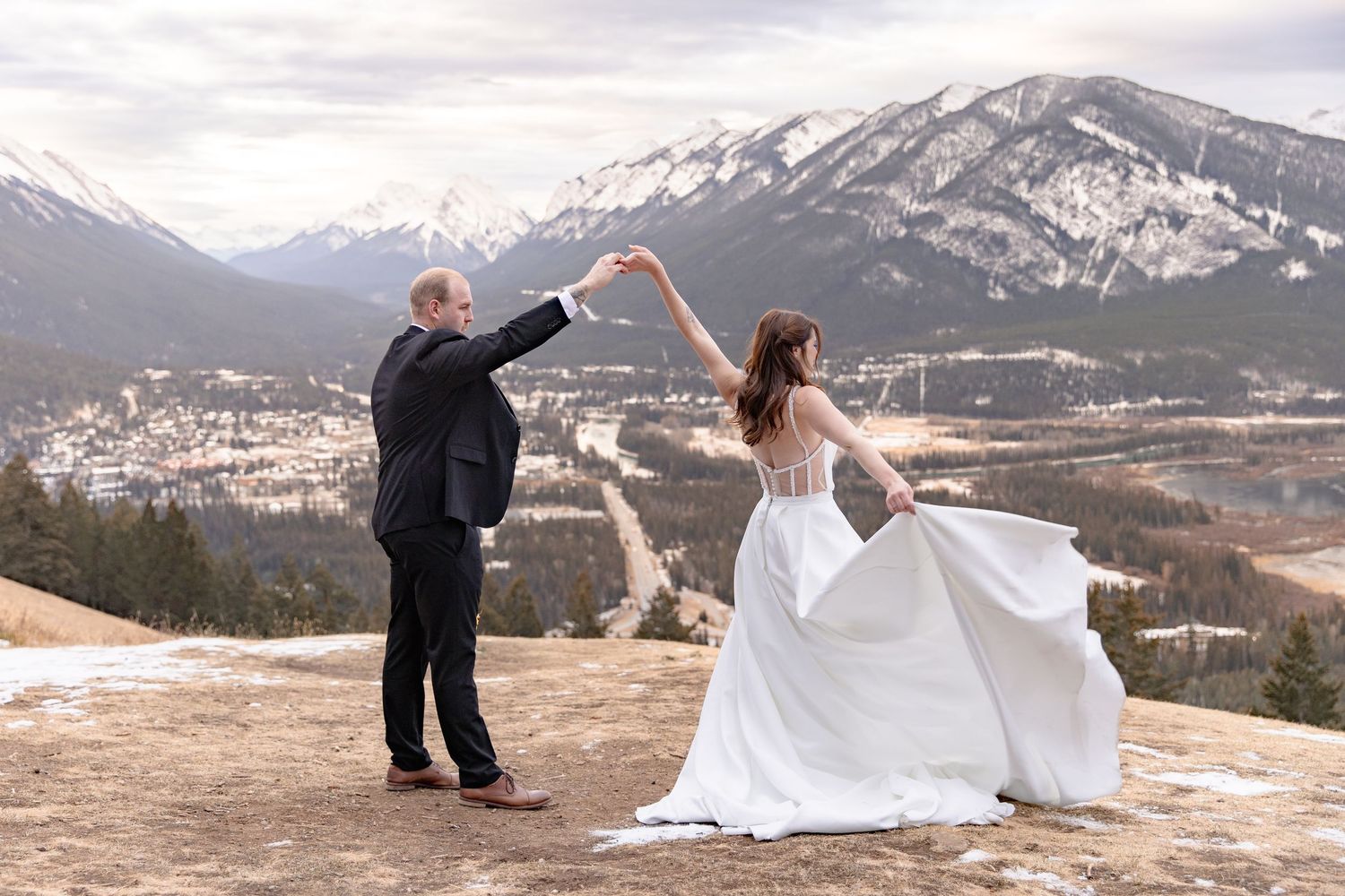 A romantic winter wedding photoshoot with snow-capped mountains and dramatic cloudy skies in the background.