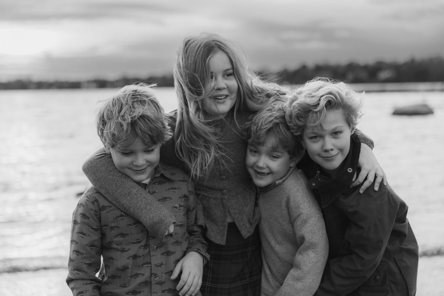 A family embraces and laughs together outdoors in black and white photography.