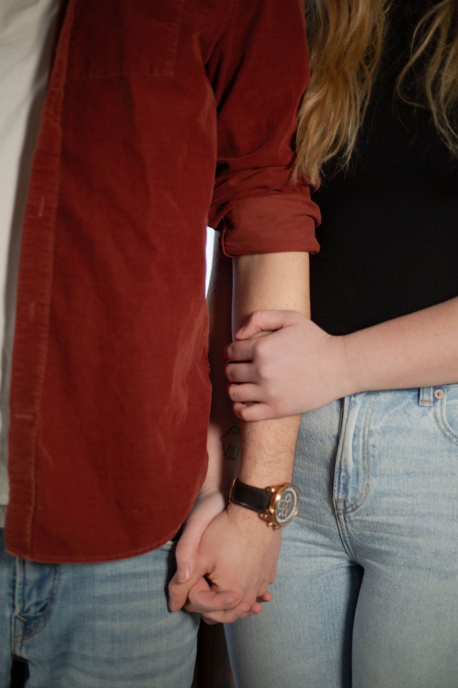 Close-up of two people holding hands while wearing casual clothing and jeans.