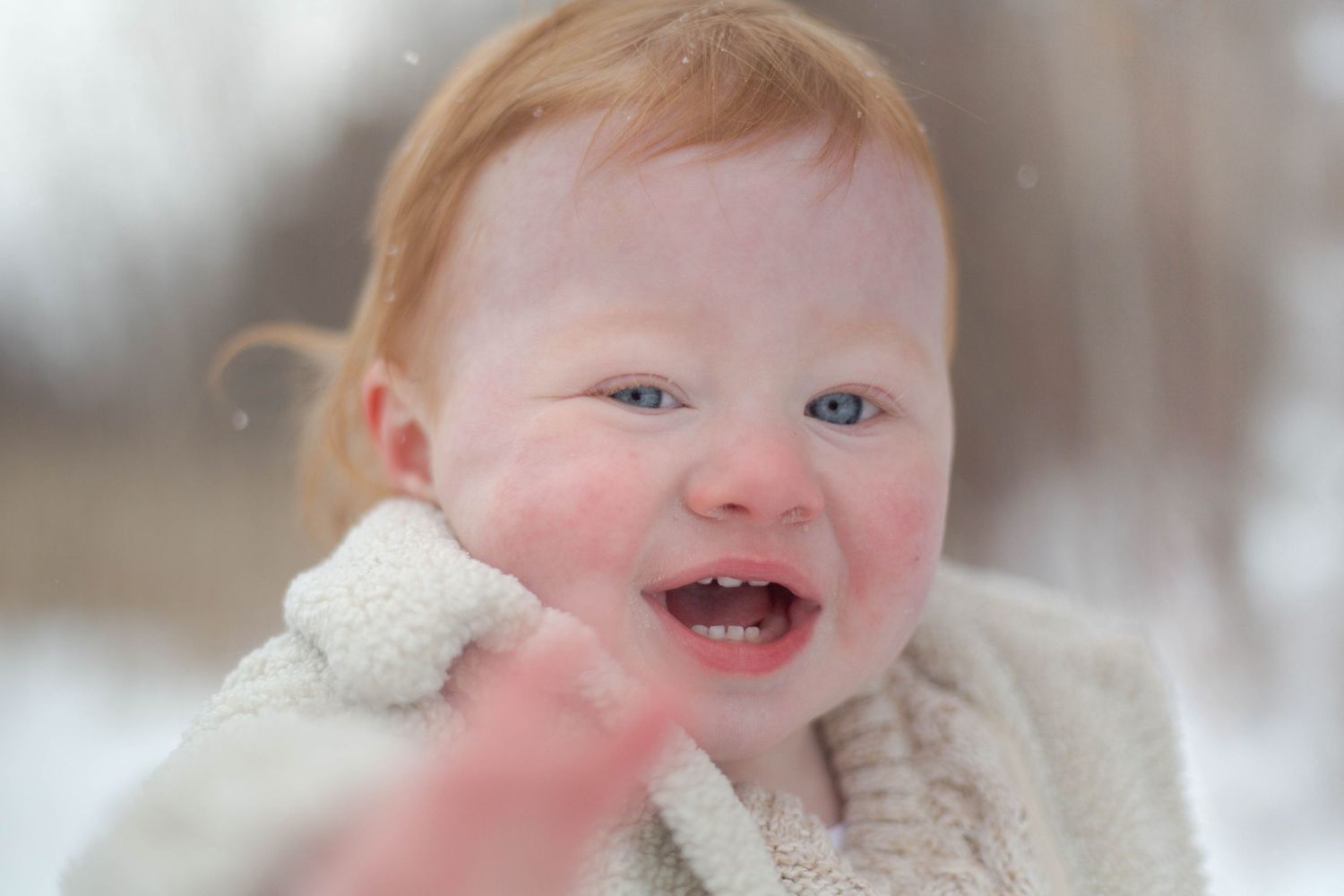 Happy baby with rosy cheeks laughs while wearing a cozy white winter outfit.