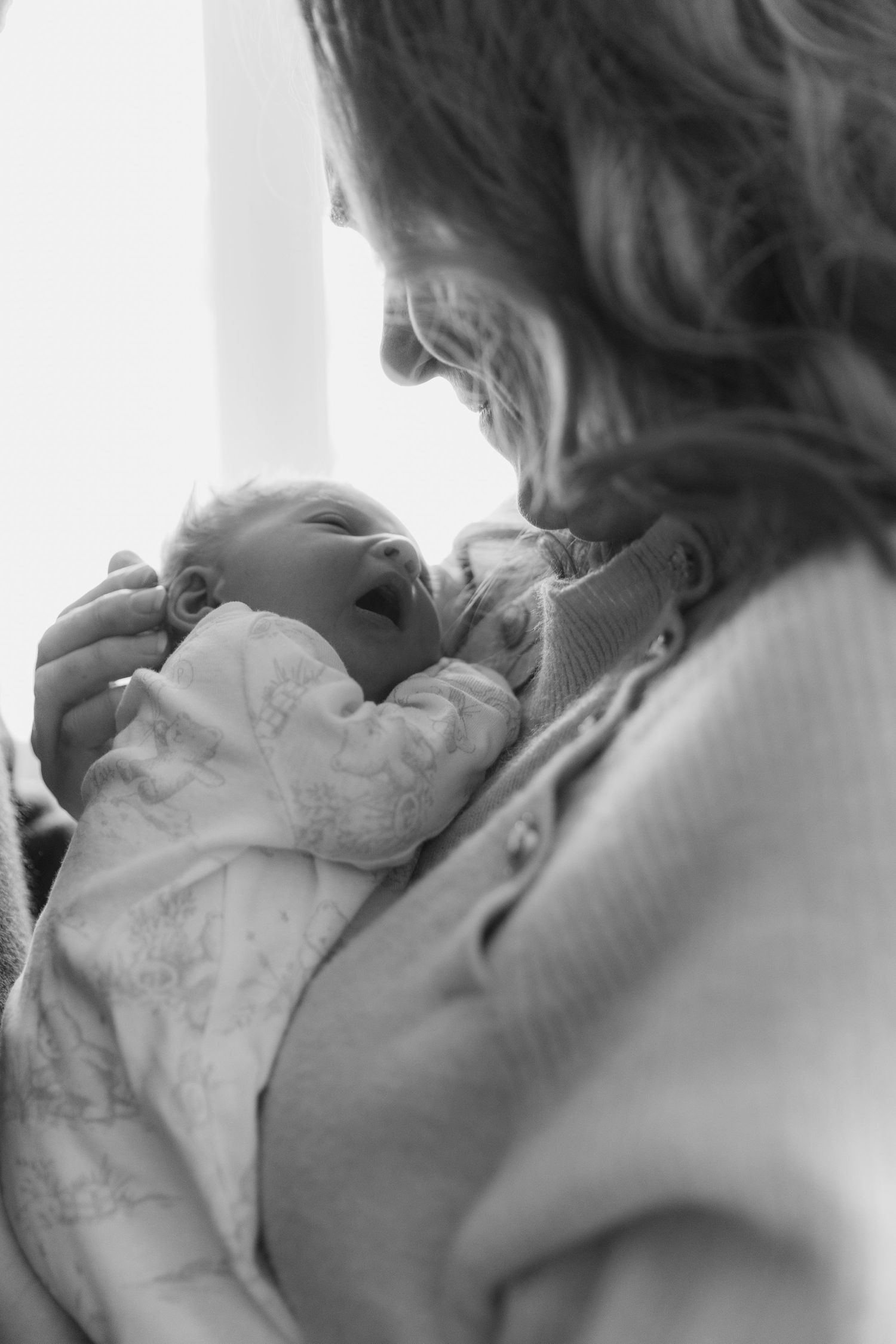 A tender moment between caregiver and infant in white christening attire captured in black and white.