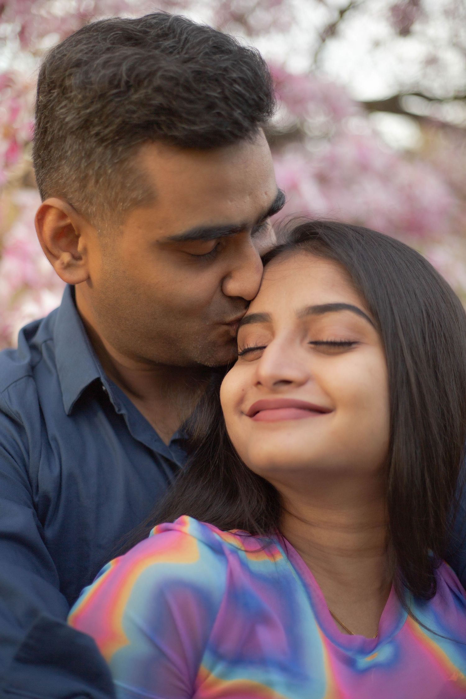 A romantic couple shares an intimate moment among blooming pink cherry blossoms in springtime.