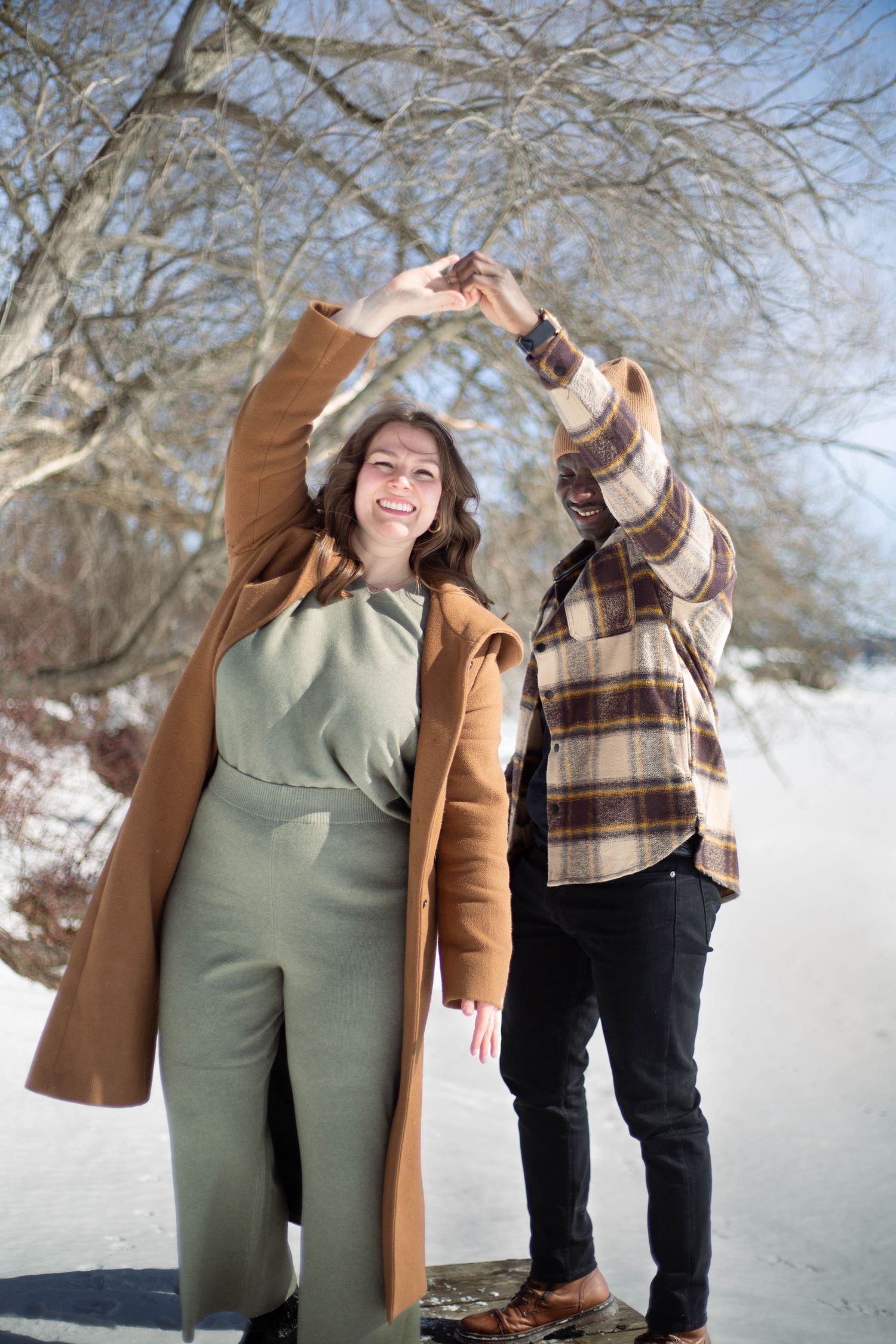 A couple dances together in the snow, holding hands up in a playful pose.