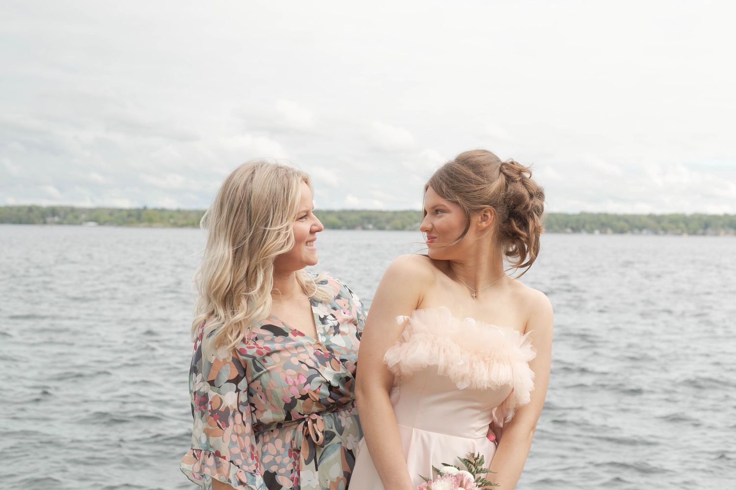 Two people share an intimate moment by the water in romantic spring attire.