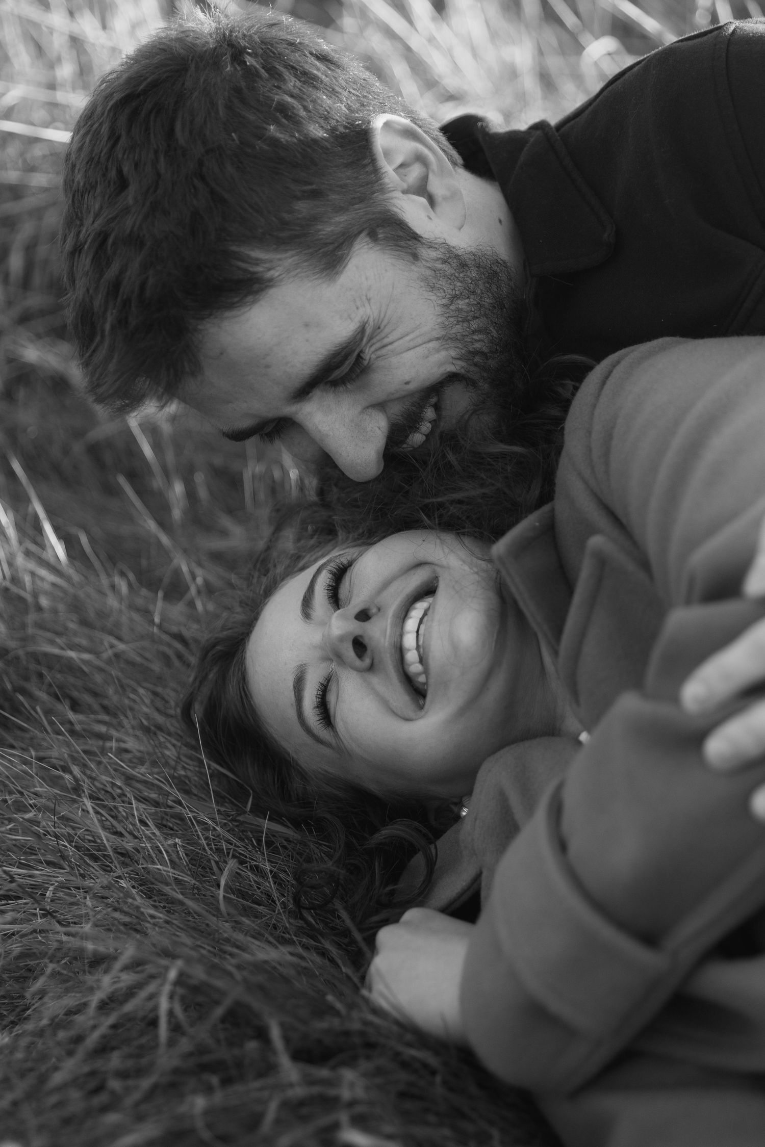 A series of black and white photos showing joyful, candid moments of laughter while lying in tall grass.