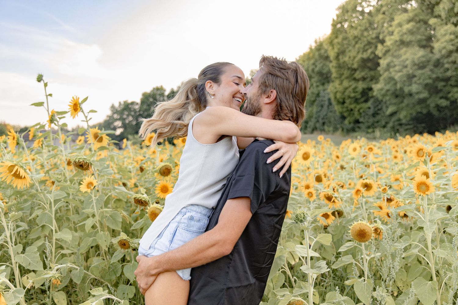 A couple shares a romantic embrace in a vibrant sunflower field during golden hour.