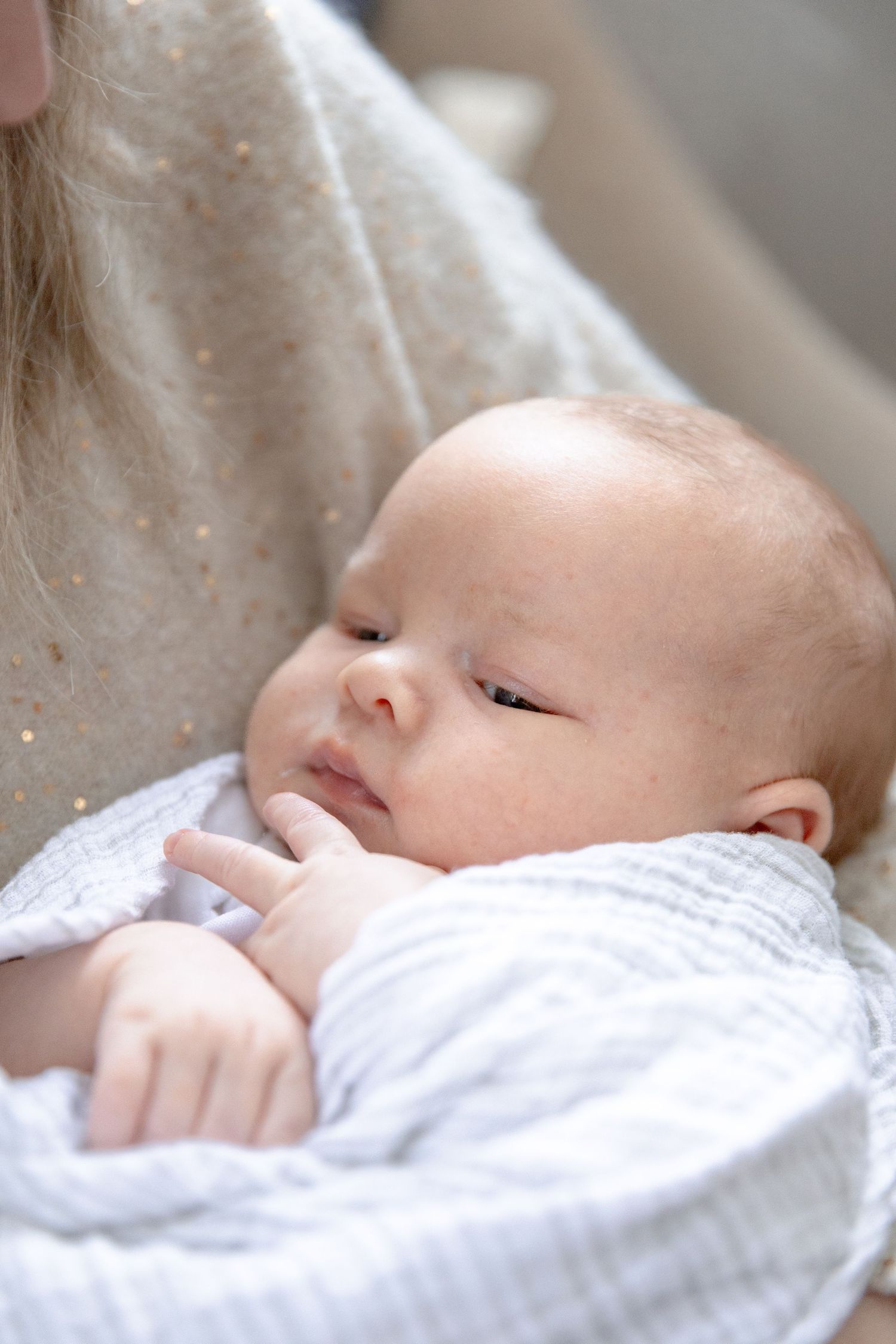 A peaceful sleeping newborn baby wearing white clothing rests against a soft blanket.