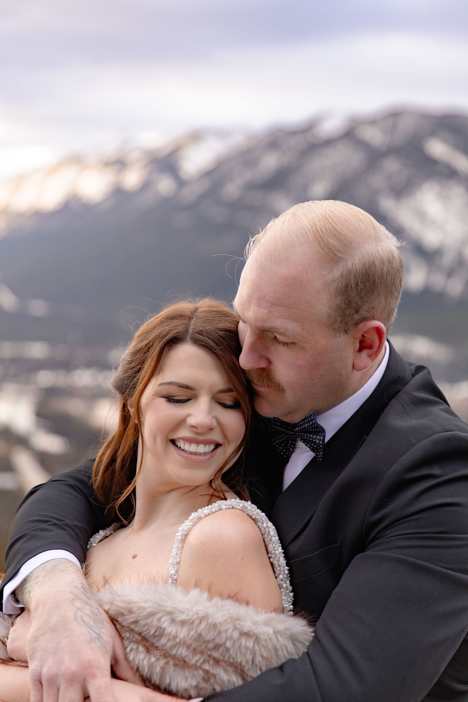 Romantic wedding couple sharing intimate moments against a snowy mountain backdrop during sunset.