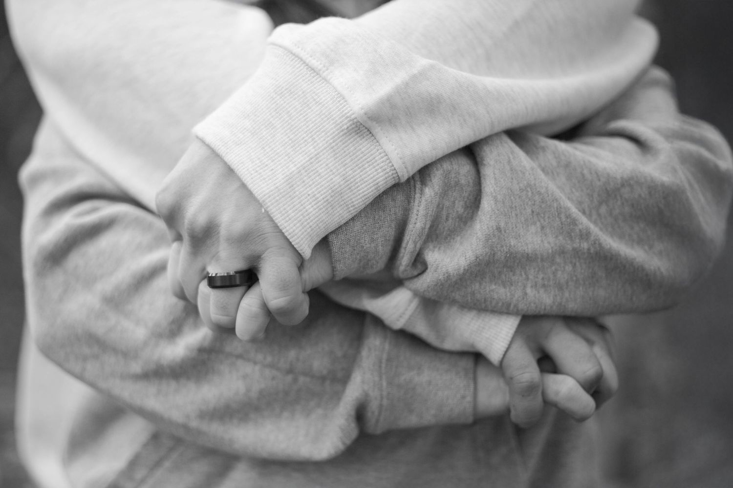 Close-up black and white image of clasped hands wearing gray sweatshirts.