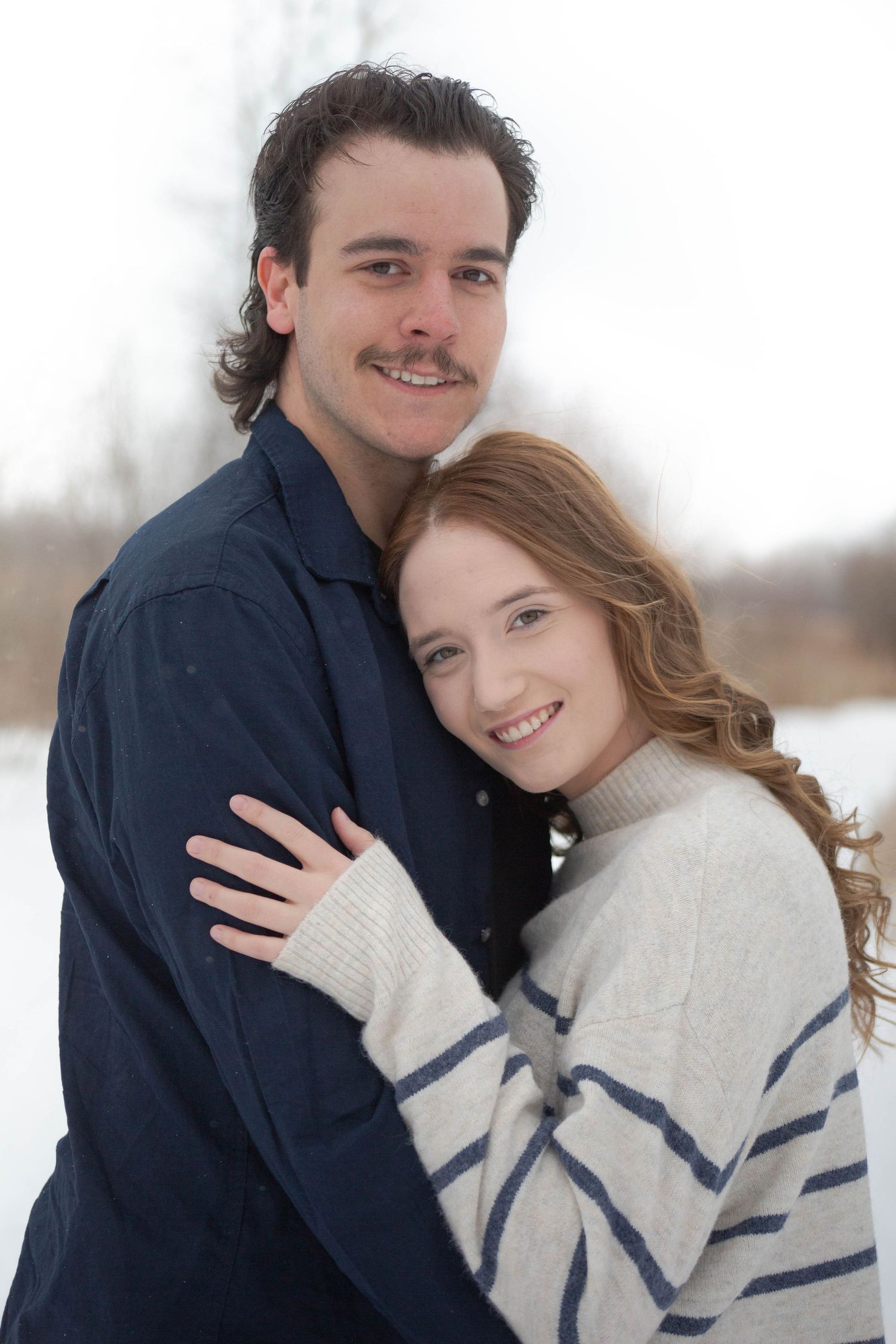 A cozy winter engagement portrait of a couple in matching navy and cream colored outfits.