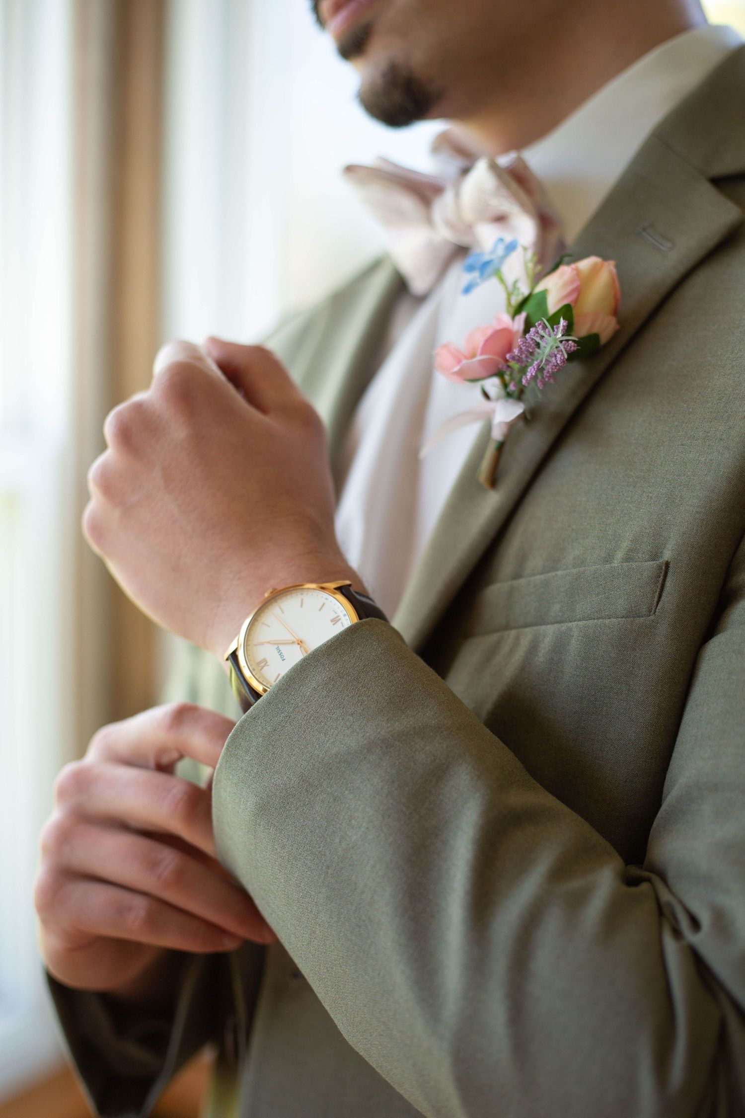 Close-up of groom in grey suit adjusting sleeve while wearing wristwatch and peach rose boutonniere.