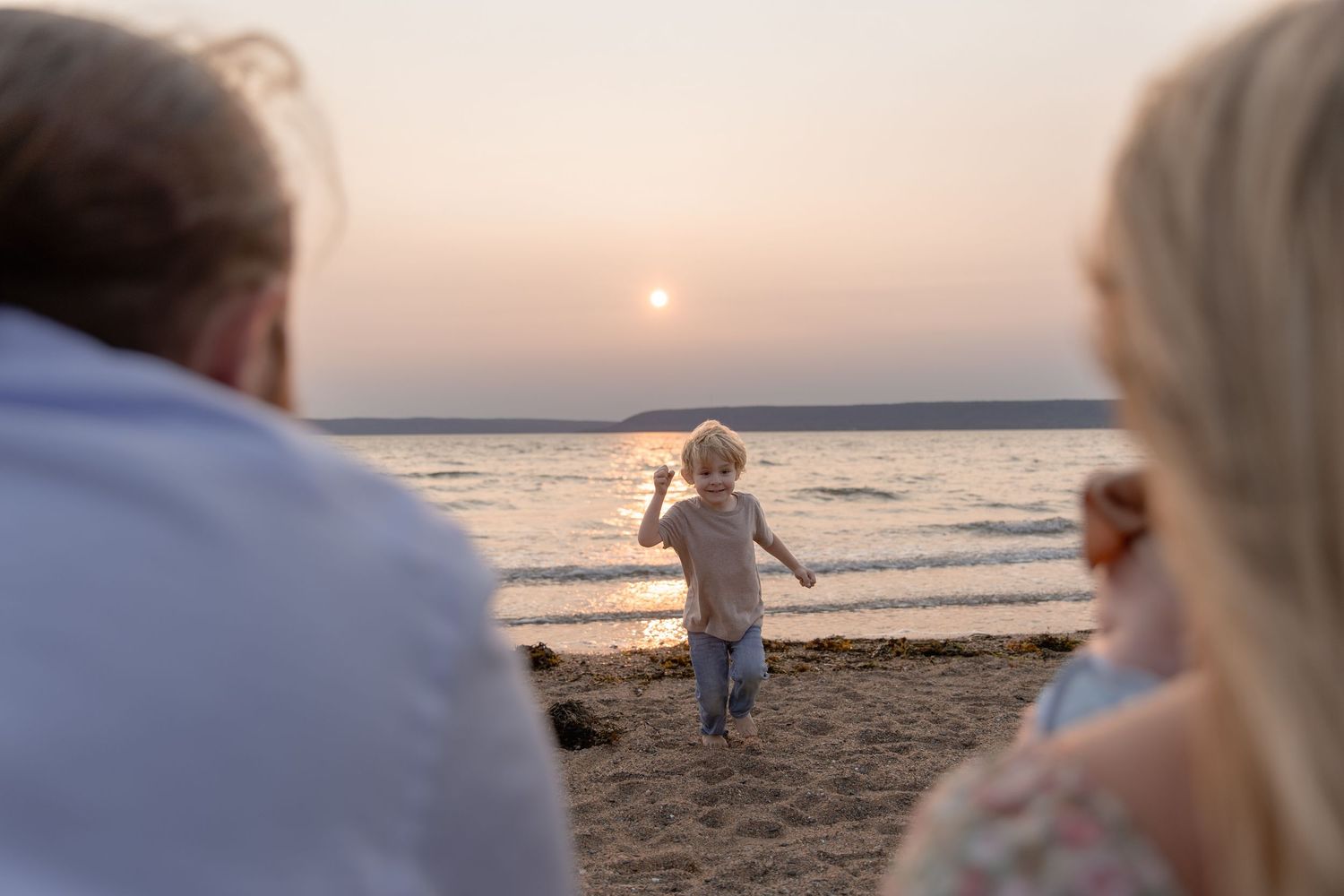 Silhouettes of people walking and standing along a sunset beach with orange skies reflecting on the water.