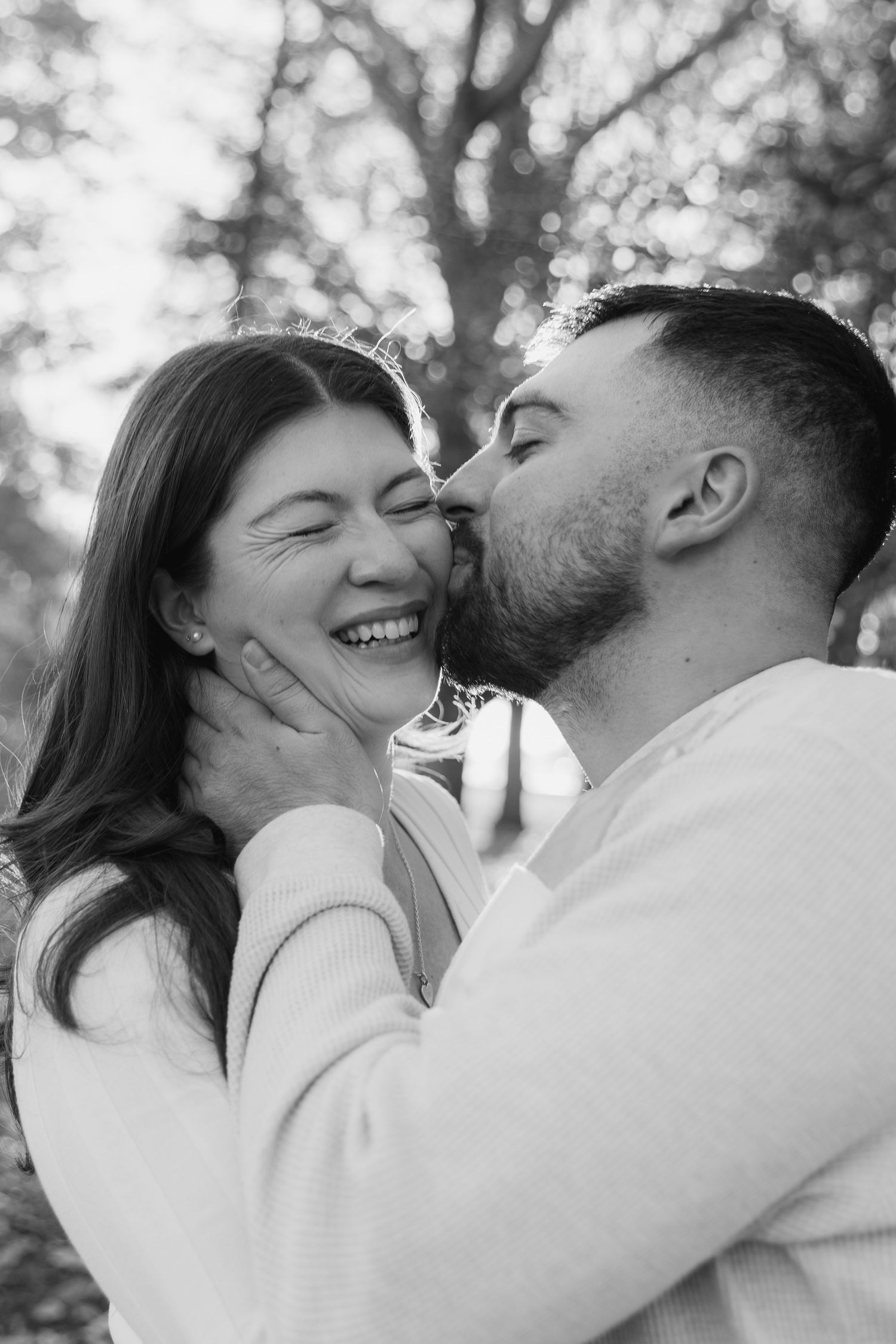 A romantic black and white photo series showing a couple sharing intimate kisses and laughter in an outdoor setting.