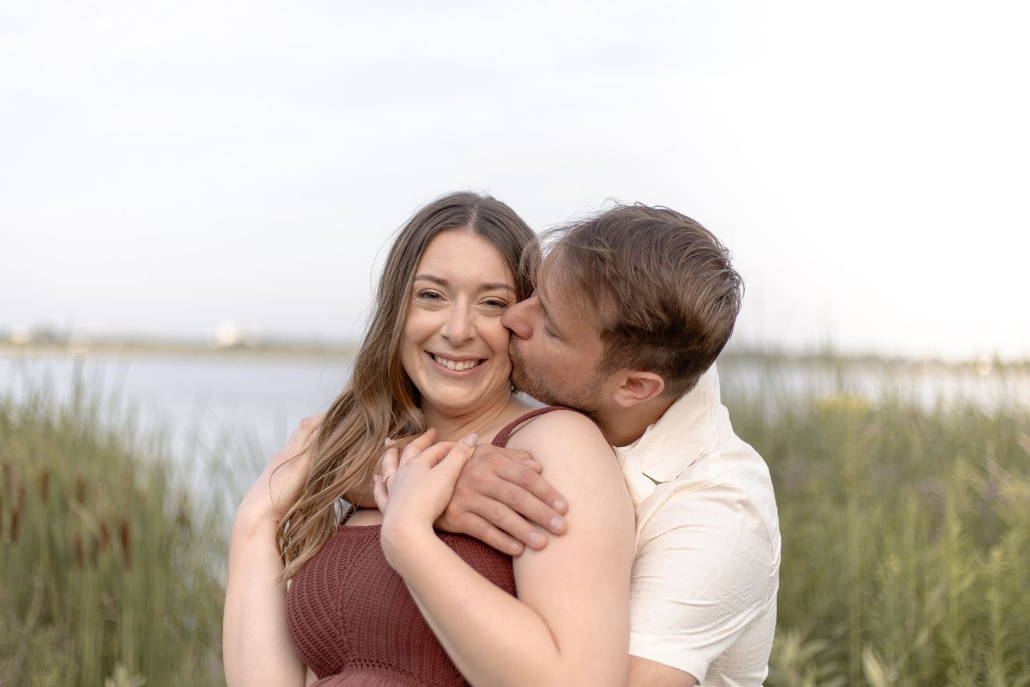 A couple embraces lovingly in a field of tall grass during golden hour at sunset.