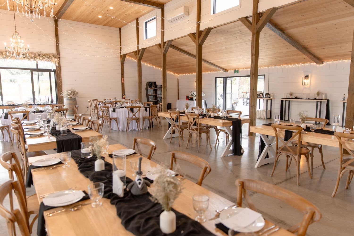 Modern rustic event venue interior with wooden beams, white walls and elegant table settings for a wedding reception.