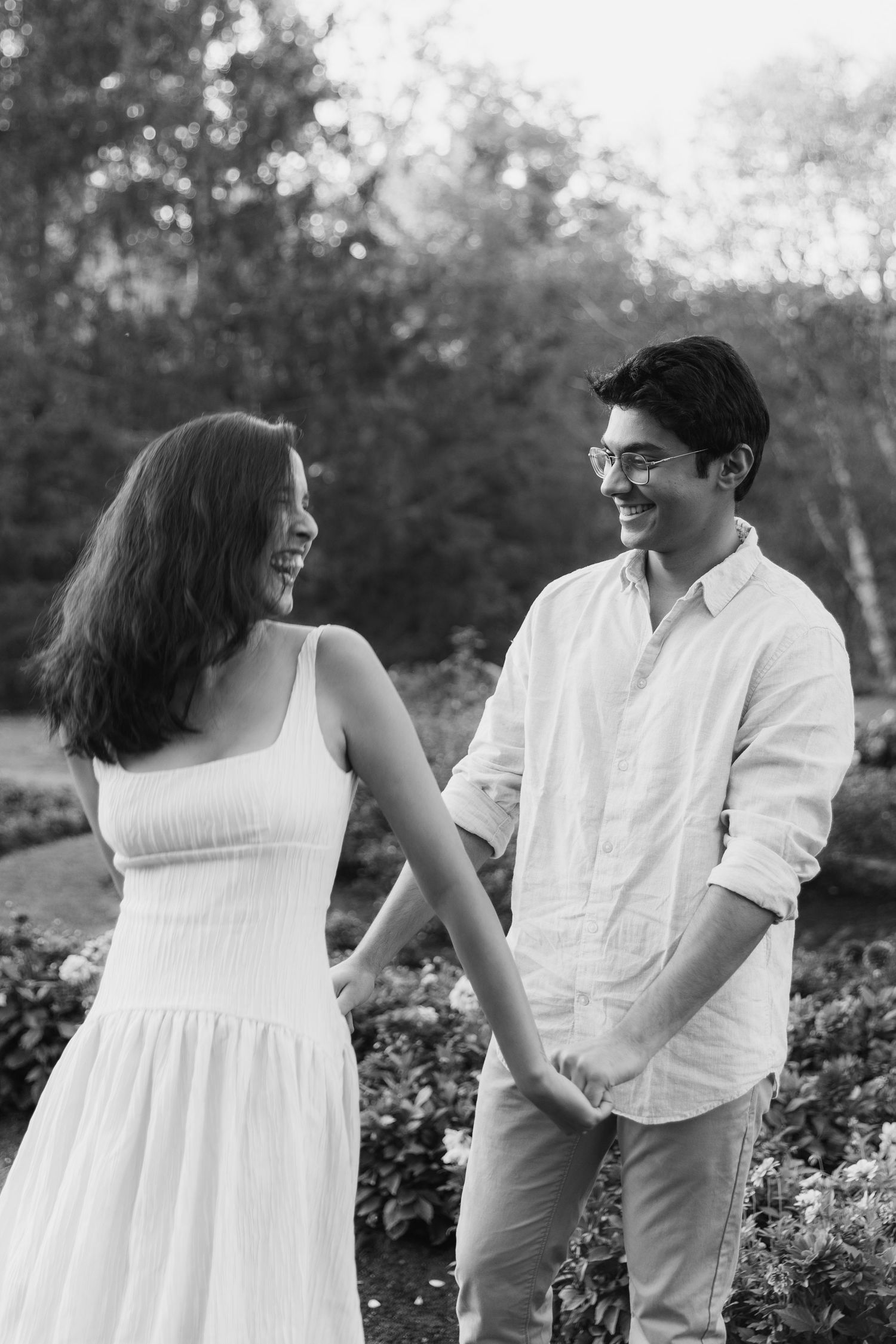 A couple shares joyful moments together in a garden setting wearing coordinated white outfits.