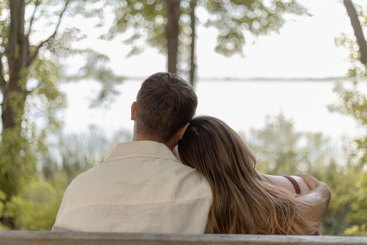 A romantic couple embraces on a beach at sunset with soft golden light and ocean waves in the background.