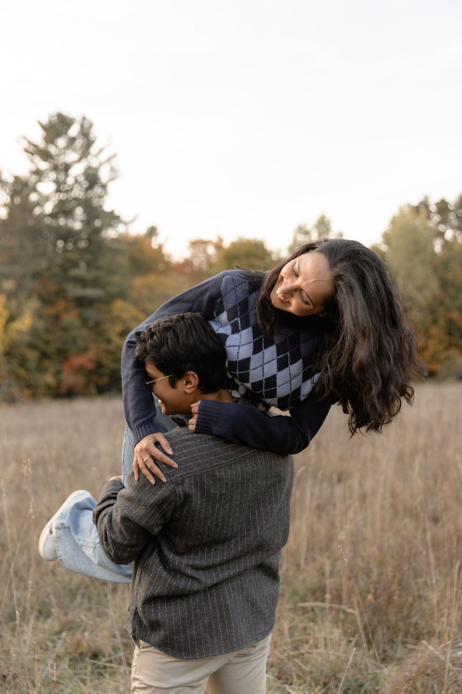 A couple embraces in a playful dip pose while standing in a golden autumn field at sunset.