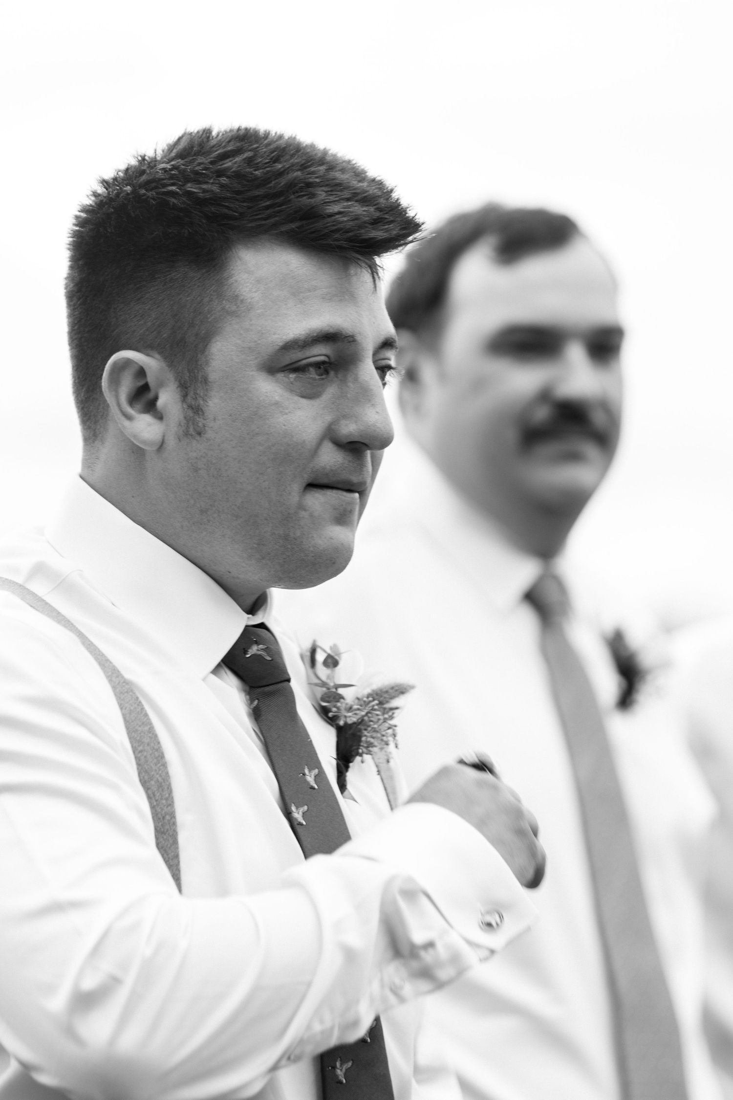A row of groomsmen in white tuxedo jackets stand together at a formal wedding event.