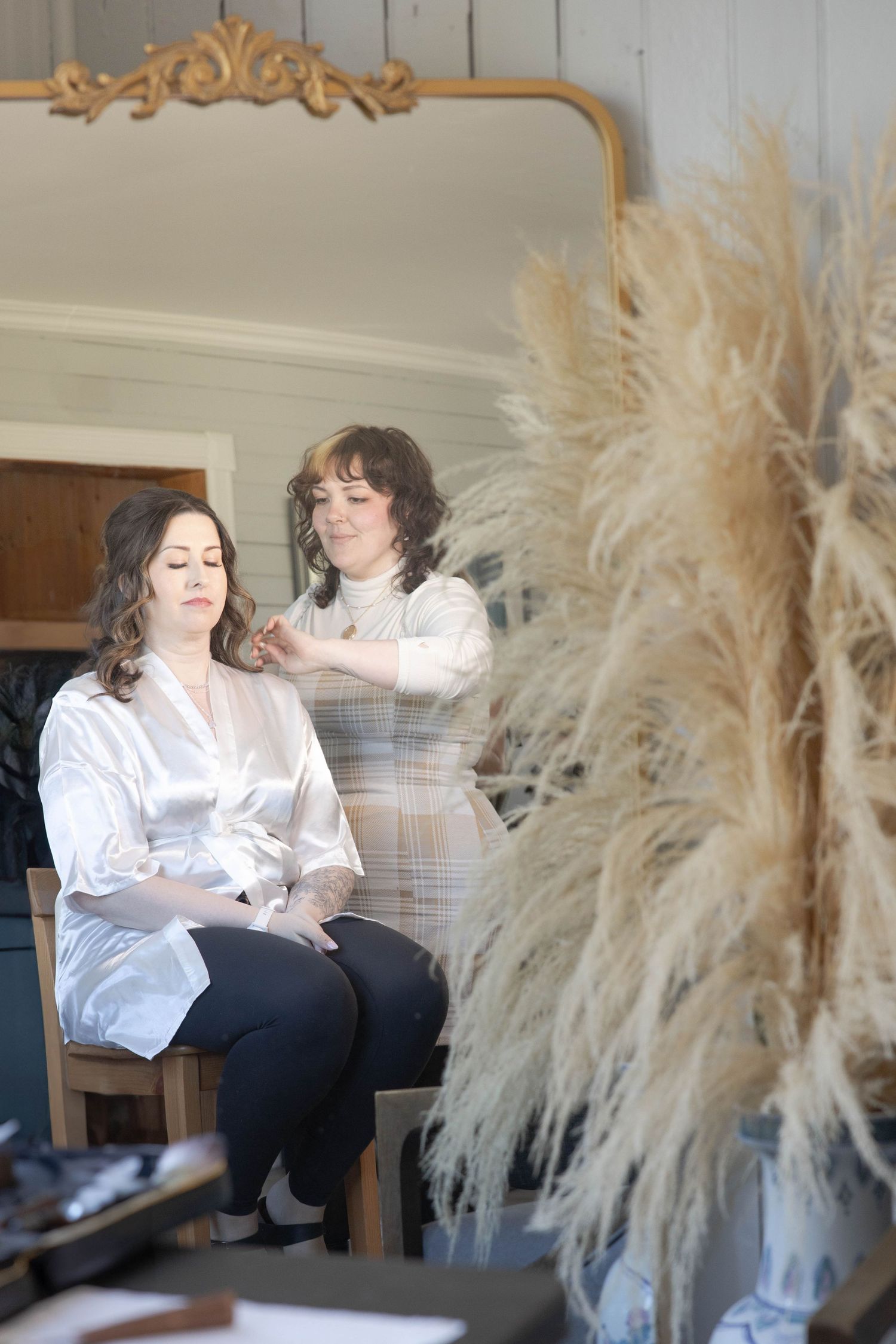 A peaceful beauty salon scene with pampas grass decor shows a stylist working on a client in a serene, white-toned setting.