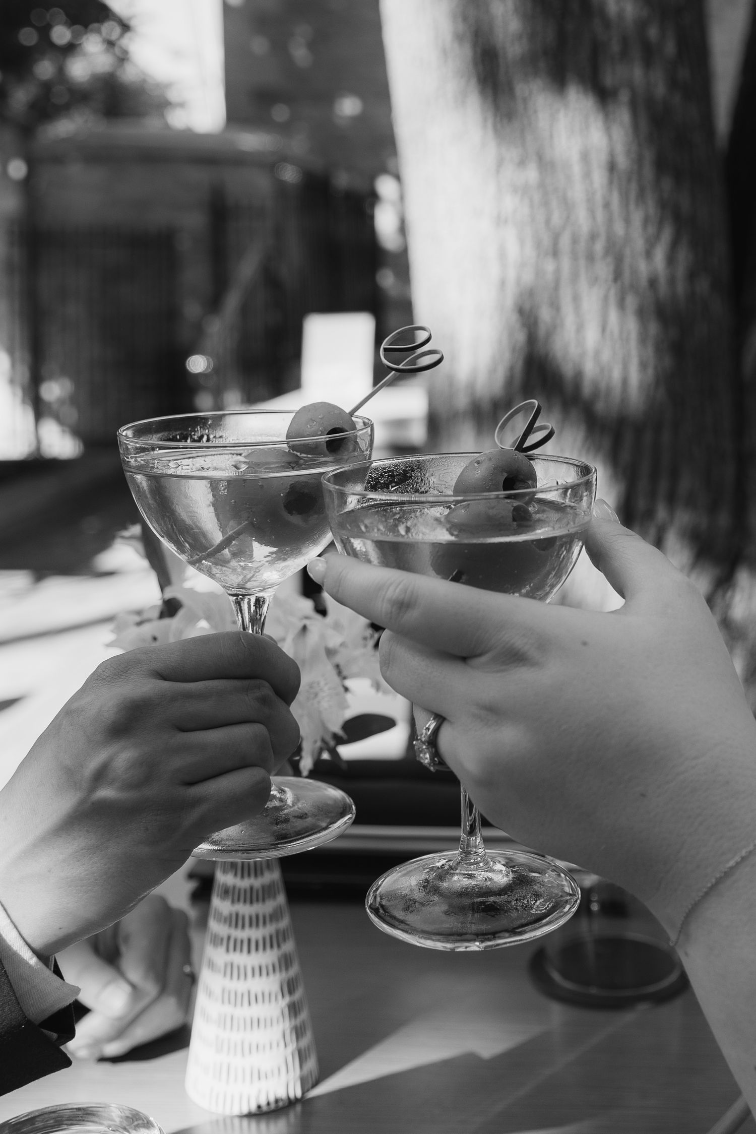 Three black and white photos show hands holding martini glasses with a miniature Leaning Tower of Pisa figure behind them.