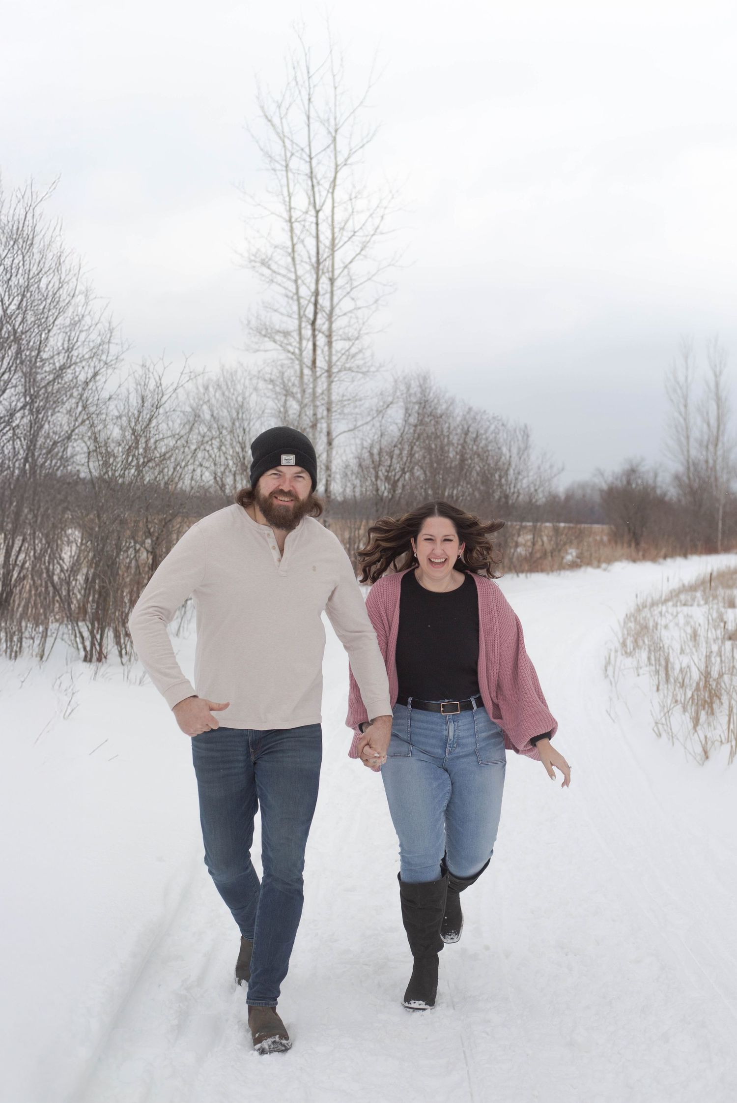 Joyful couple running together on a snow-covered path through a winter landscape.